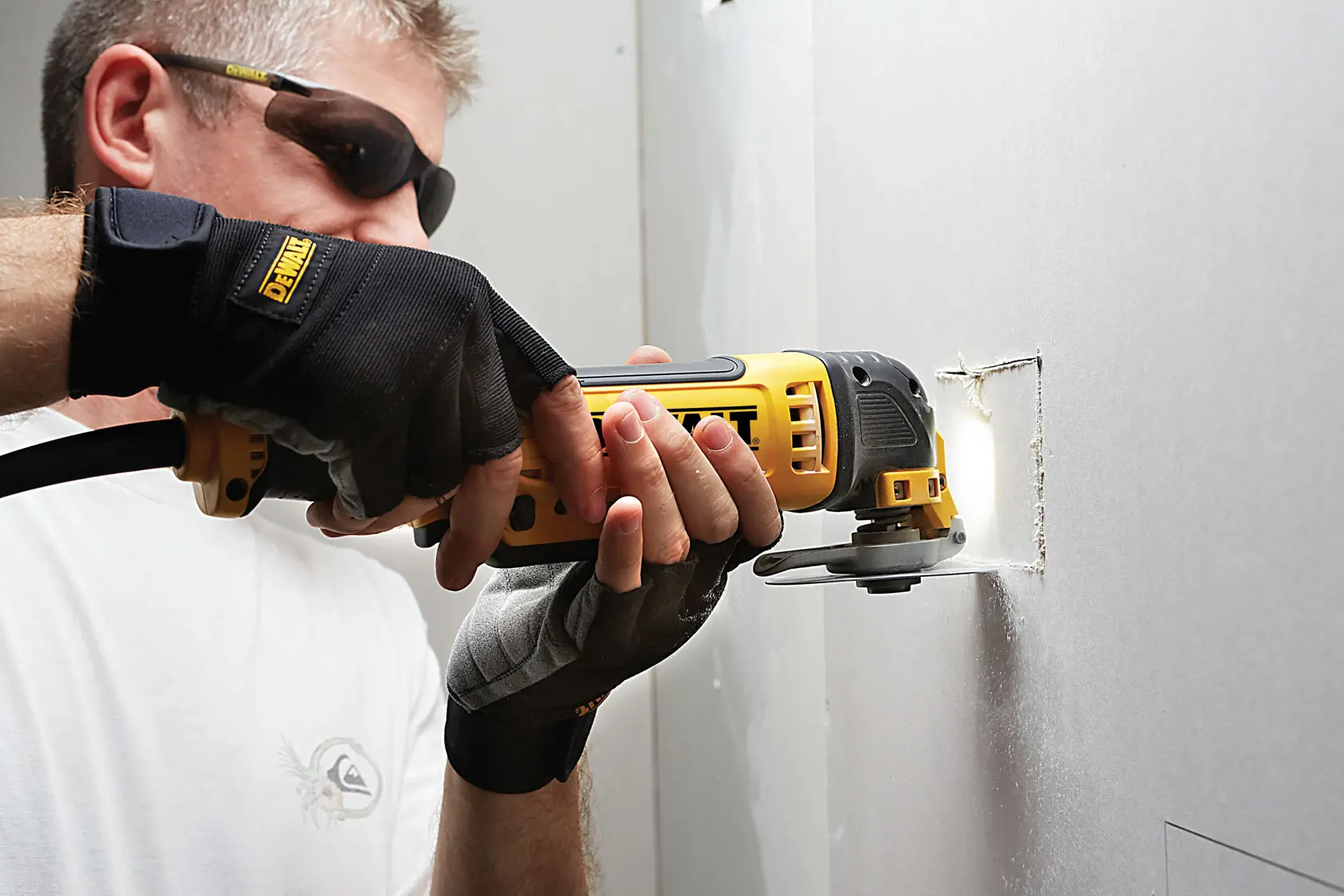 Person uses a DEWALT oscillating tool to cut a rectangular hole in a drywall panel.