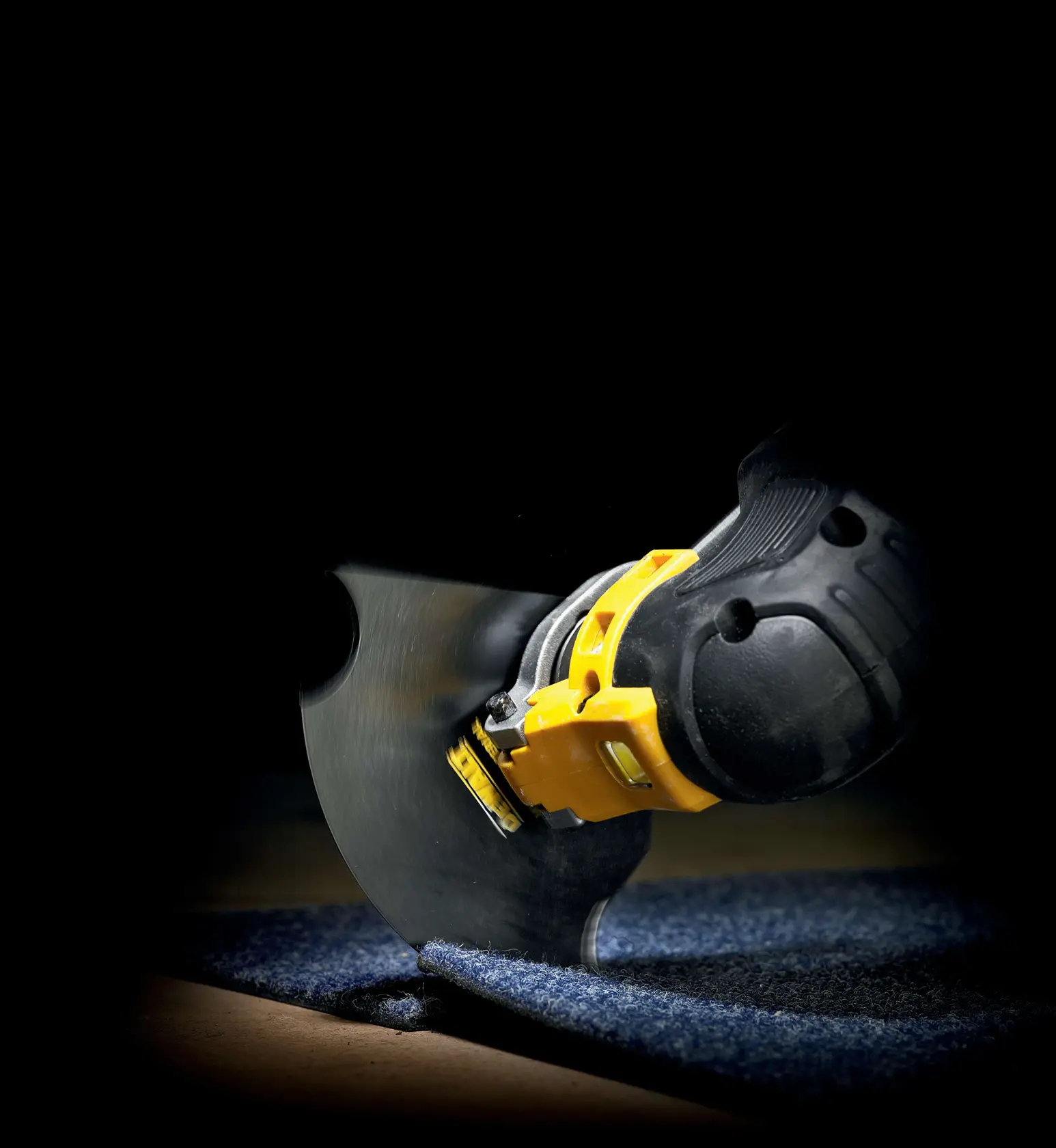 DEWALT power tool cutting through carpet with a round blade in a close-up, dark background.