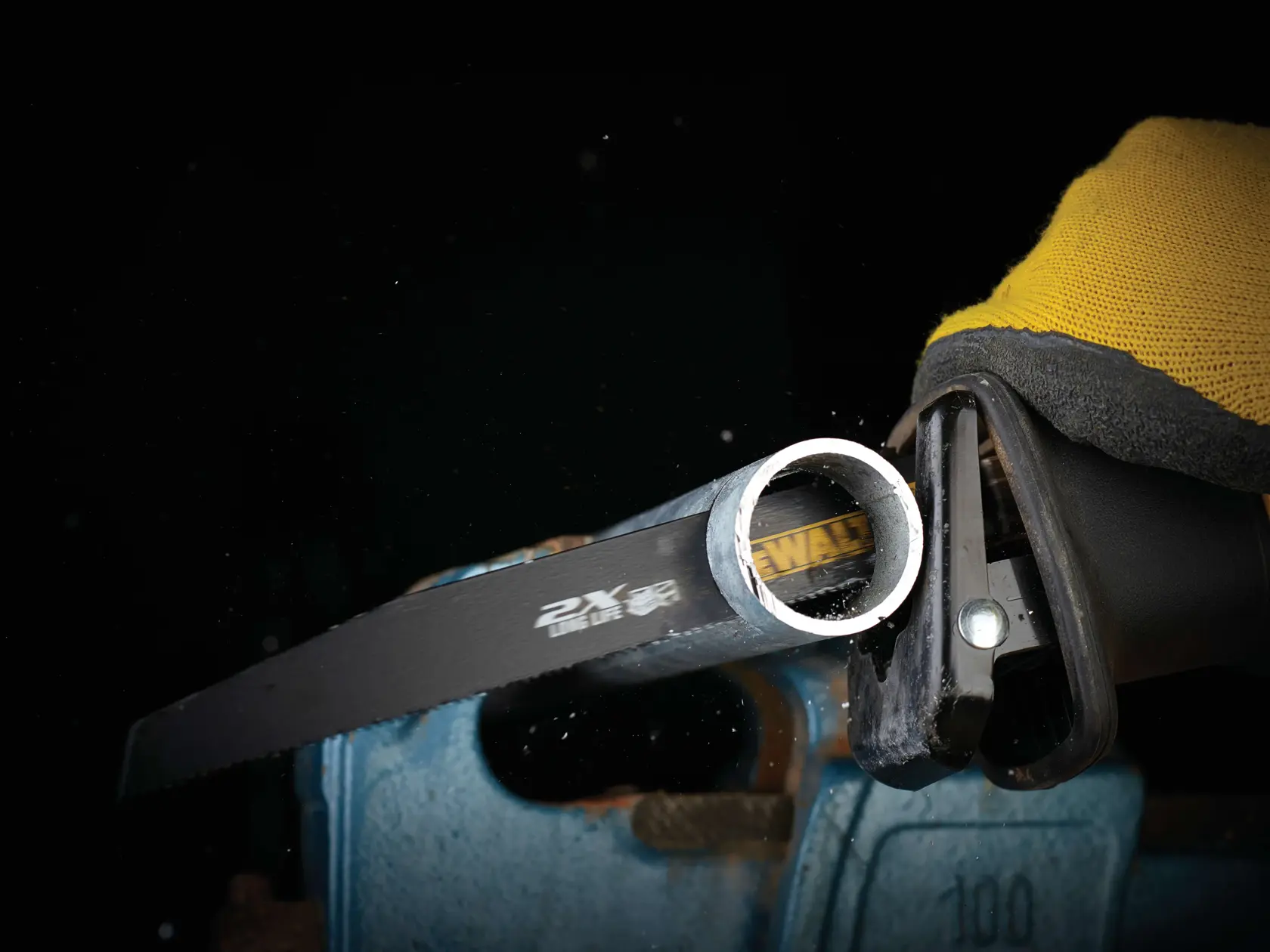 DEWALT saw blade cutting a metal pipe held in a blue vise, with a yellow-gloved hand operating the tool.
