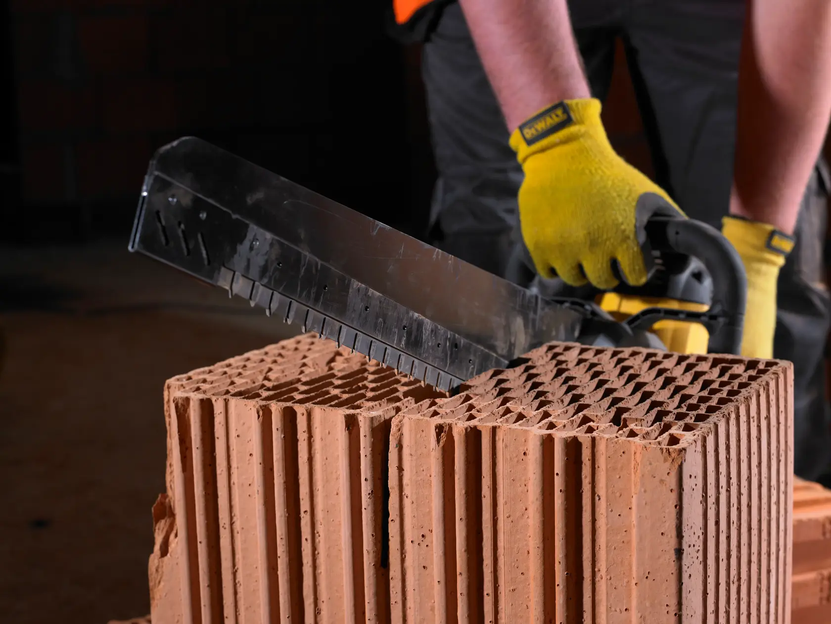 Person using DEWALT tool to cut a large, hollow brick. Tool has yellow handle and gloves are worn.