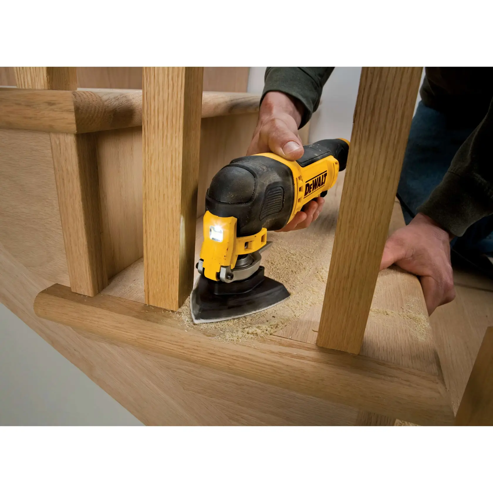 Una multi-herramienta DEWALT lija escaleras de madera manualmente, se ve polvo de madera.