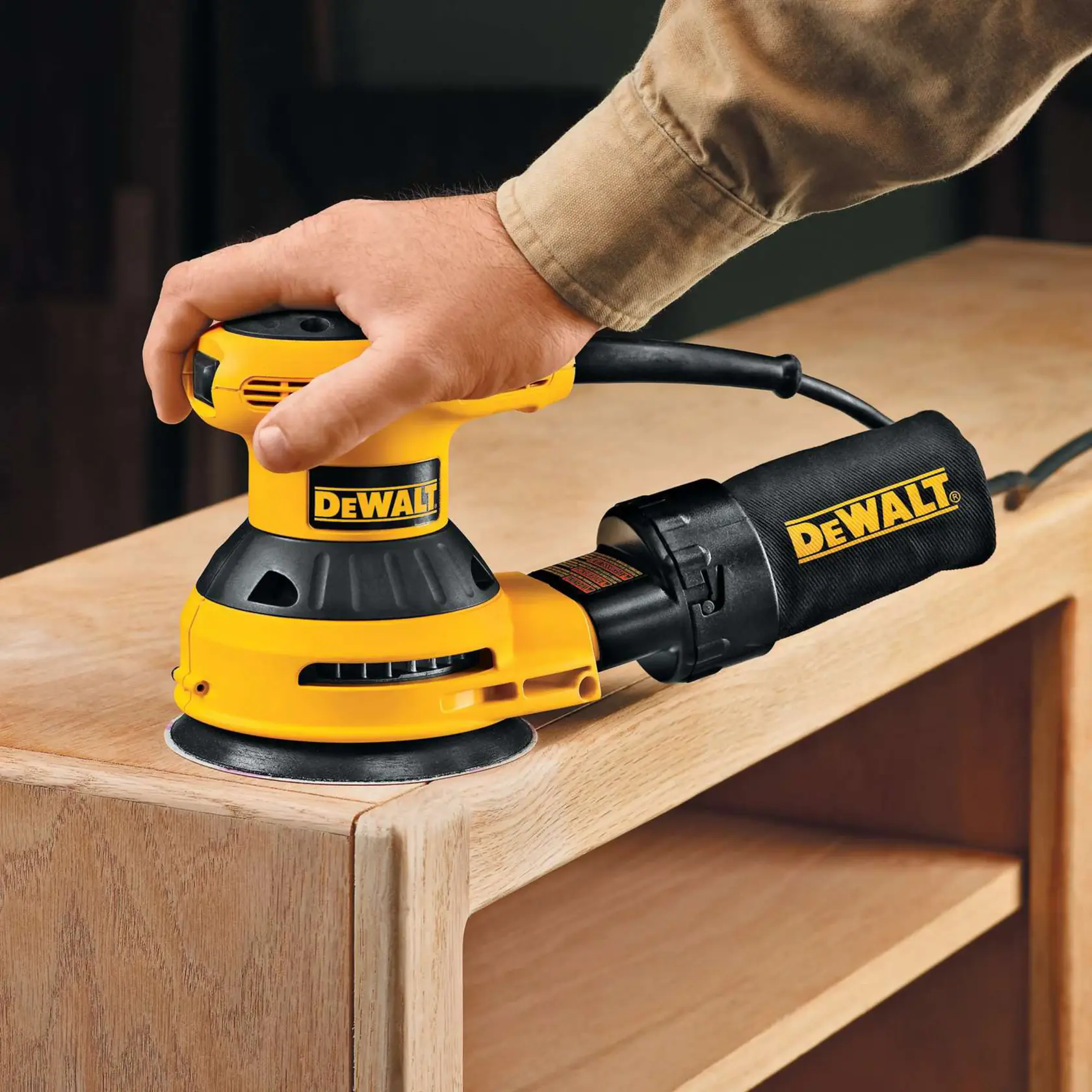 DEWALT sander in use sanding the edge of a wooden cabinet. A hand guides the yellow and black power tool.