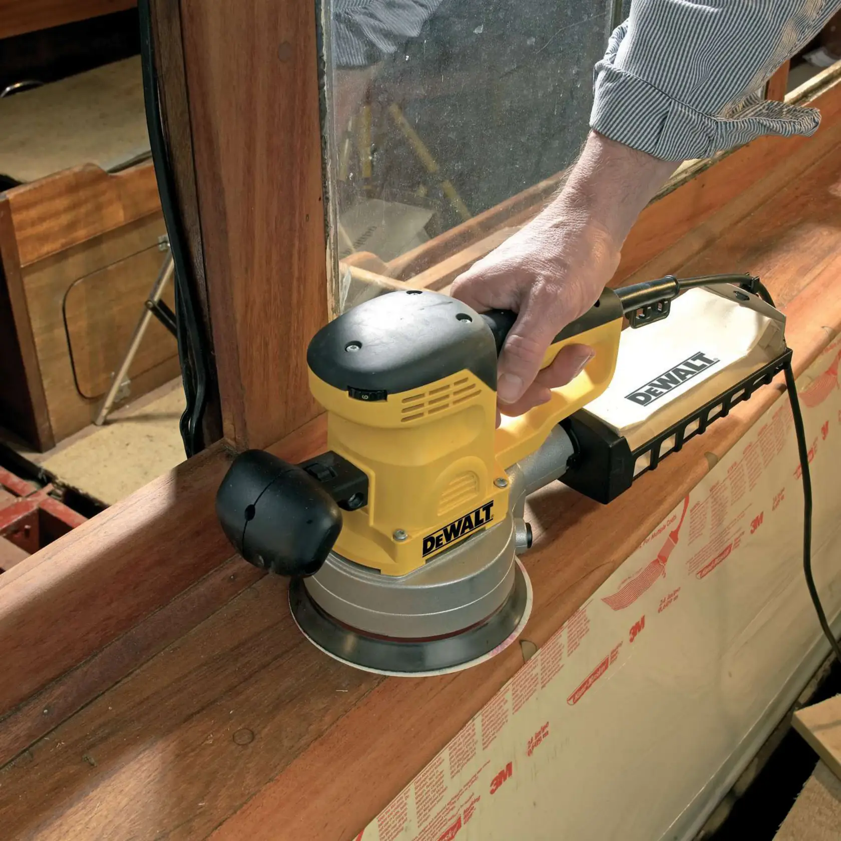 Persona usa una levigatrice DEWALT DT3123 gialla-nera su legno vicino a una finestra.