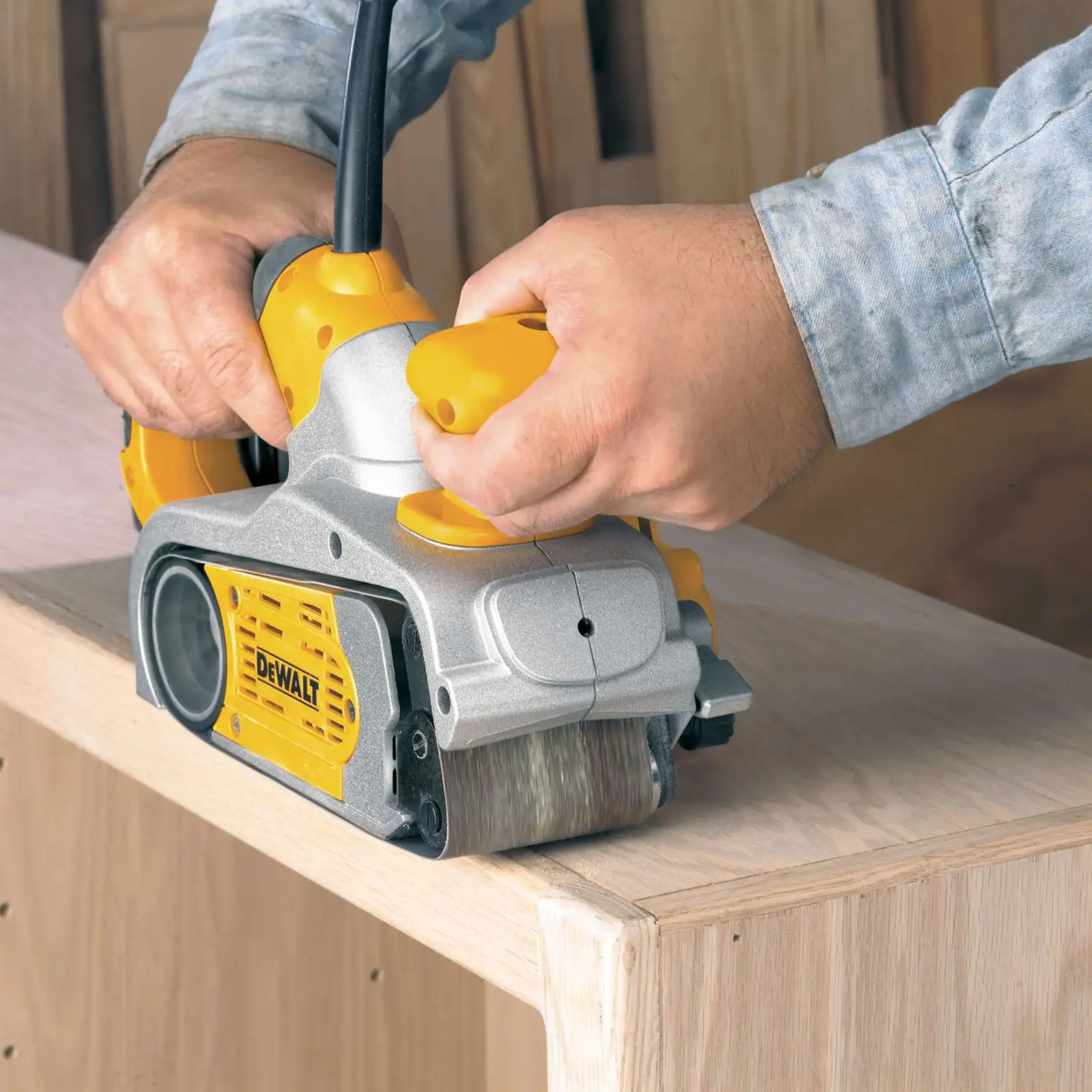 Person sanding wood with a yellow DEWALT belt sander on the edge of a wooden surface.