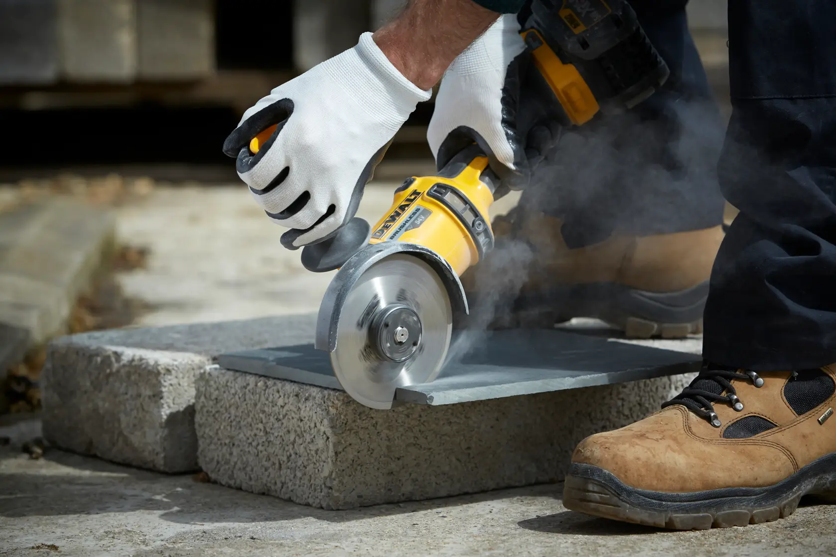 Mit Handschuhen wird draußen mit einem DEWALT Winkelschleifer Stein geschnitten und Staub erzeugt.