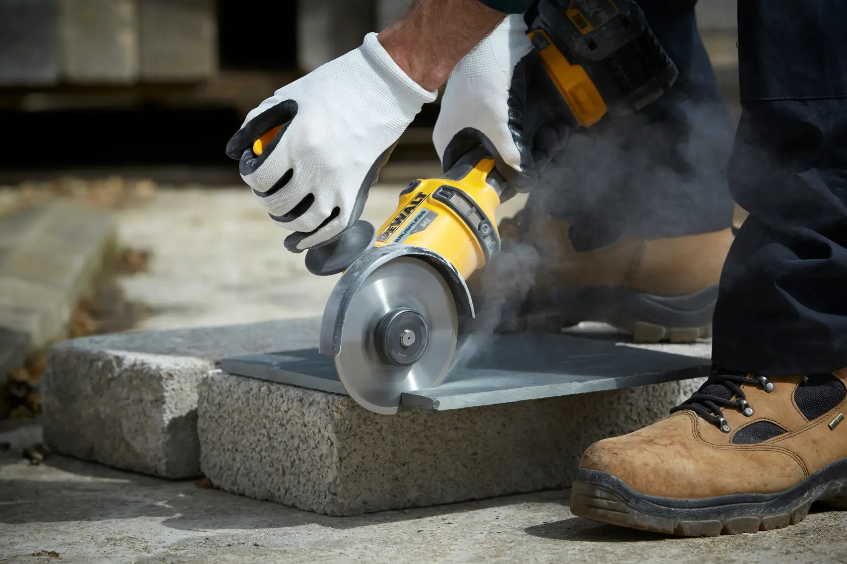 Person schneidet draußen Stein mit DEWALT Winkelschleifer, trägt Handschuhe und Sicherheitsschuhe.