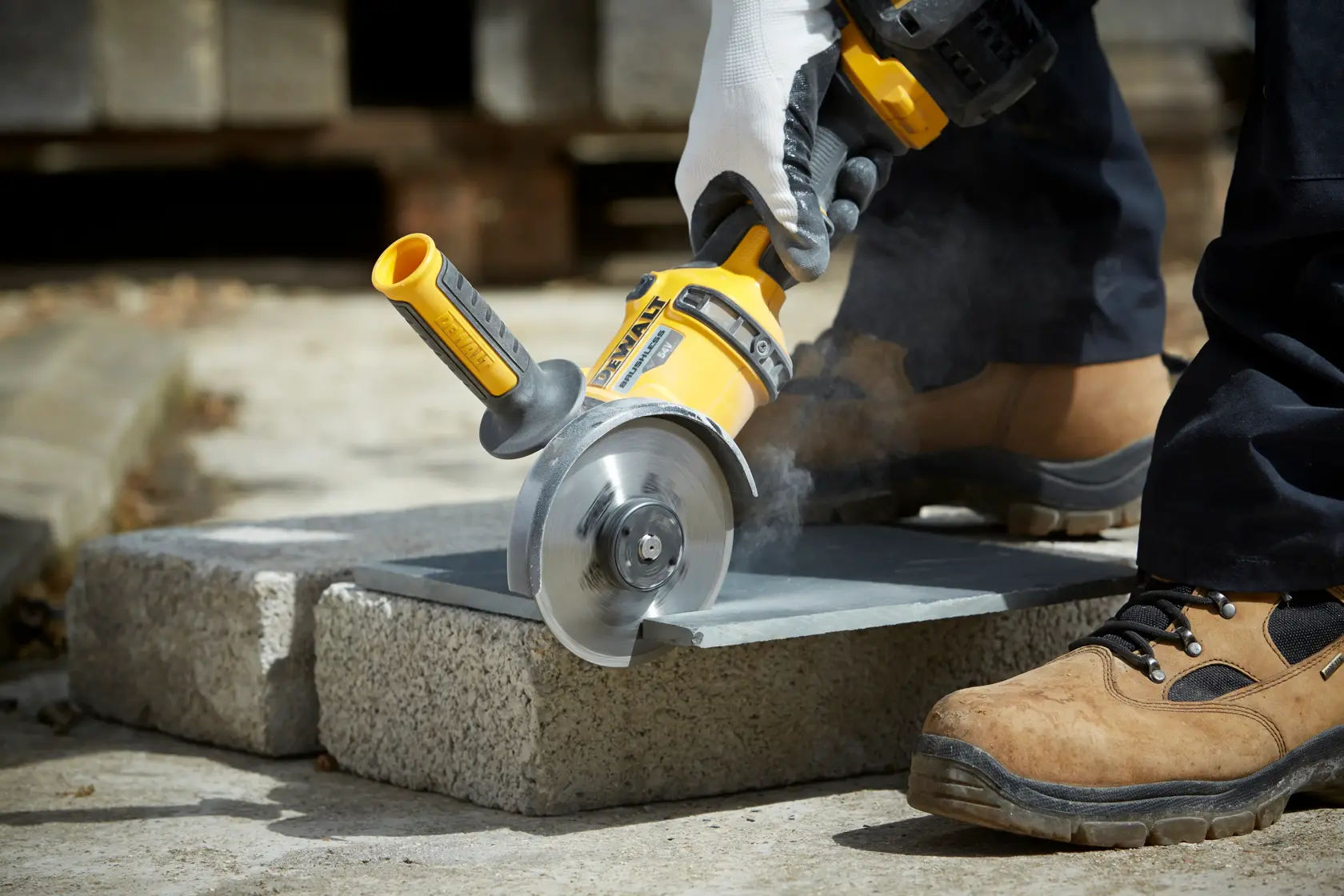 Person schneidet Steinplatte mit DEWALT Winkelschleifer, trägt Handschuhe und Sicherheitsschuhe.
