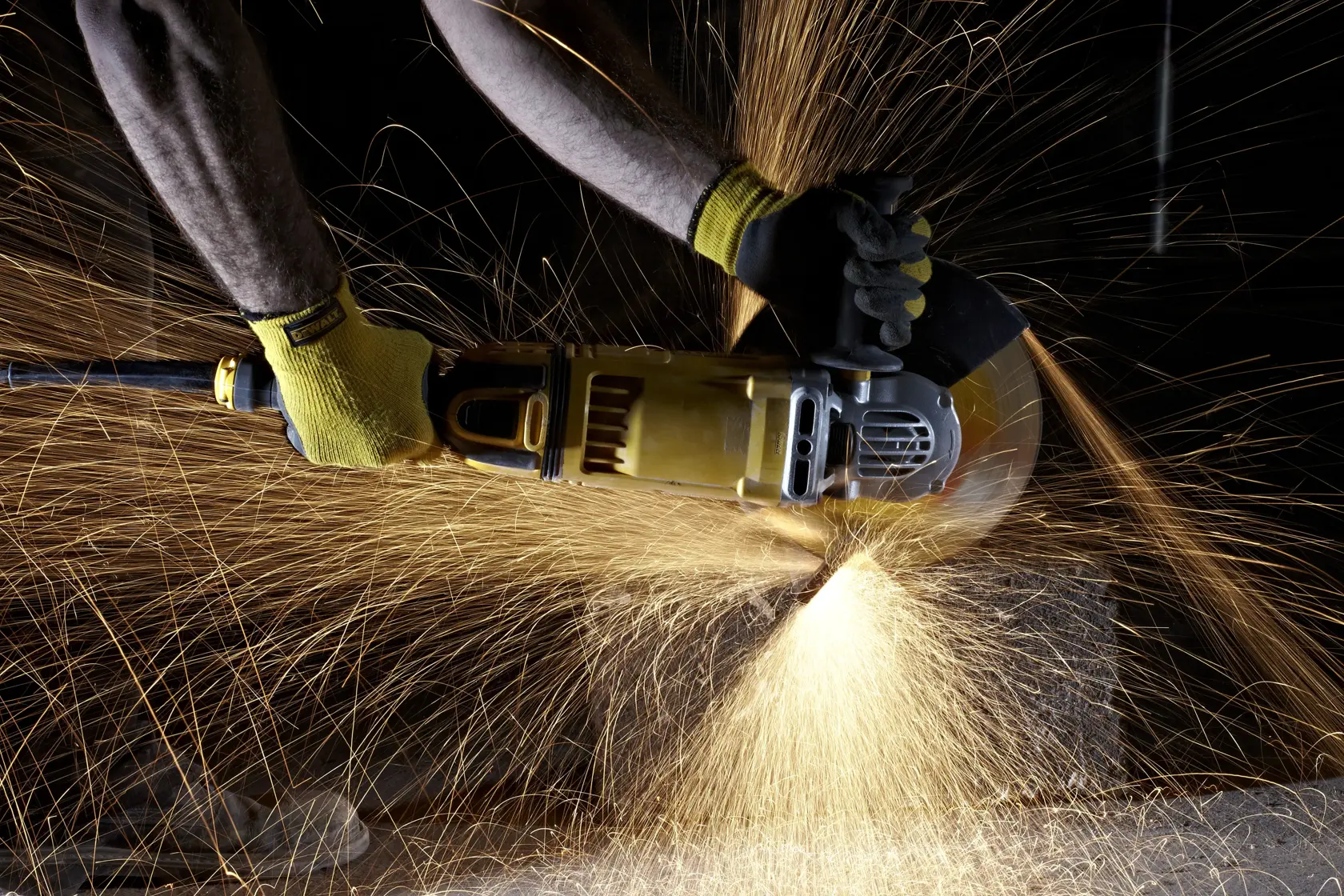 Persona usando una amoladora DEWALT genera chispas al cortar material, lleva guantes protectores.