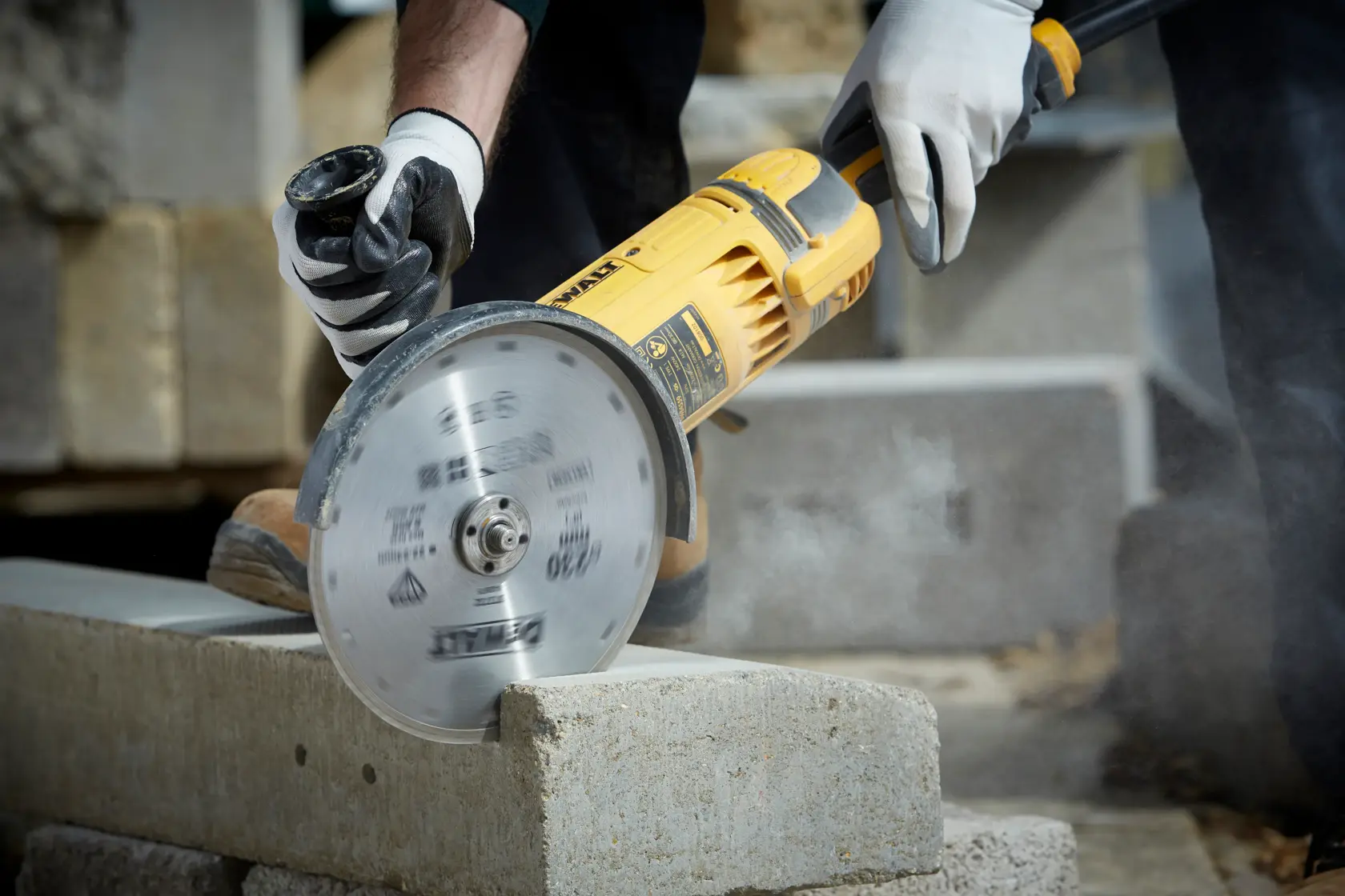 Persona corta un bloque de cemento con amoladora DEWALT y disco diamantado, usando guantes de seguridad.