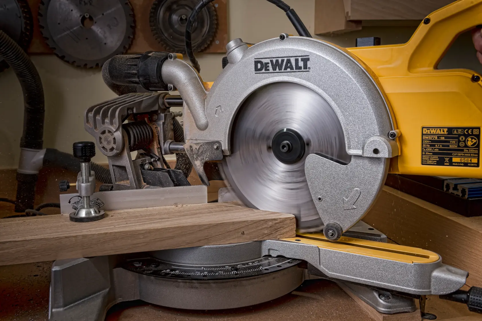 A DEWALT miter saw cutting a piece of wood in a workshop setting. The saw blade is spinning.
