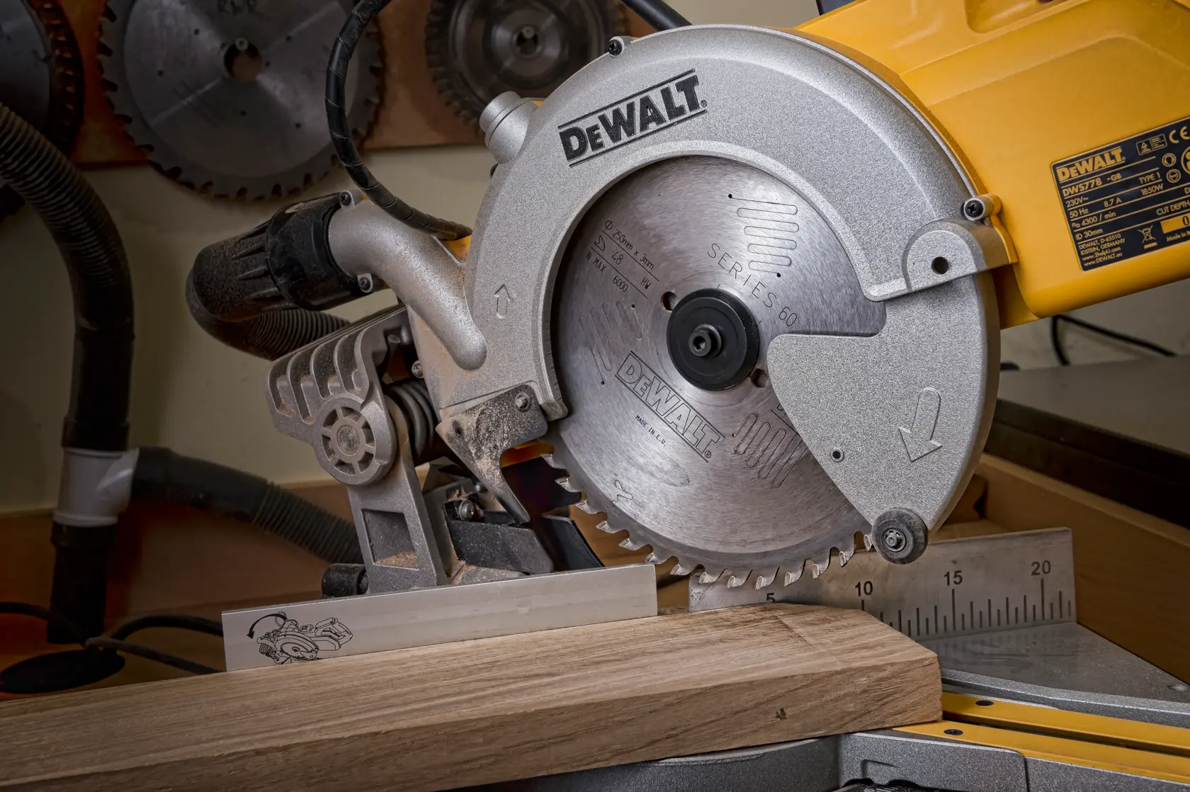 DEWALT circular saw cutting a wooden plank in a workshop, with measurement guide and other saw blades in the background.