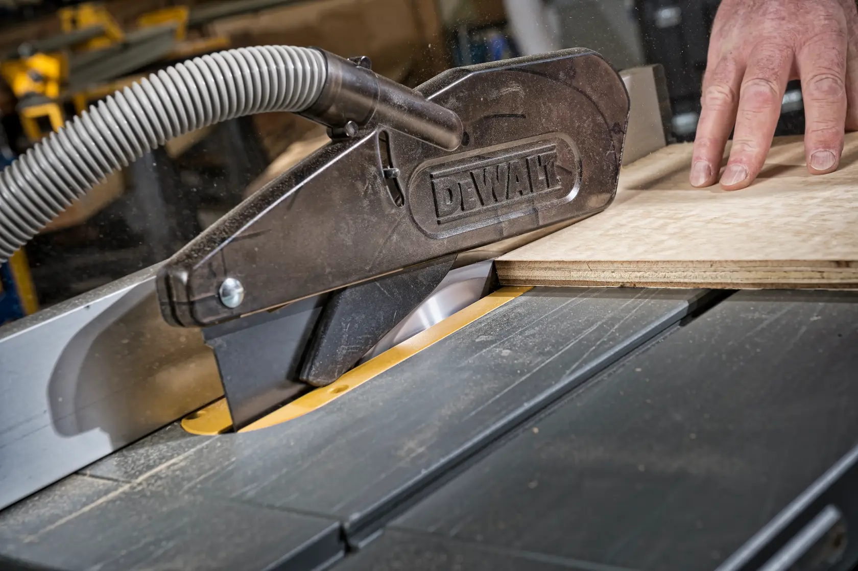DEWALT saw in use cutting wood, with dust extraction hose and hand on board.