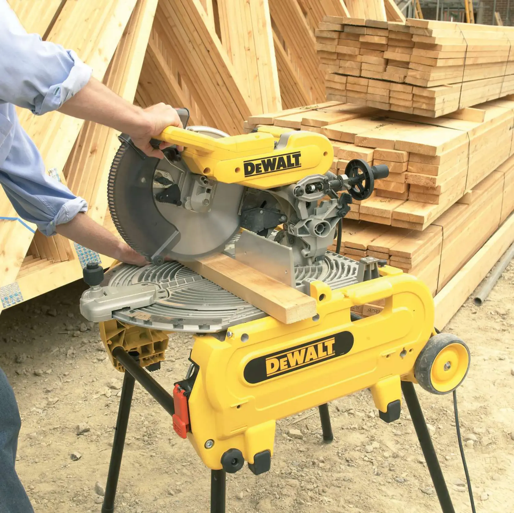 DEWALT miter saw cutting a wooden plank at a construction site with stacks of lumber in the background.