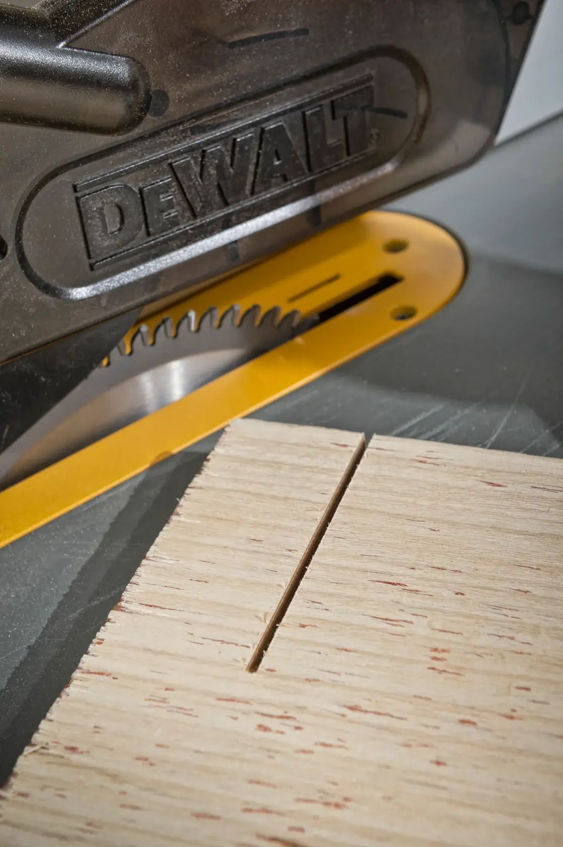 Close-up of a DEWALT saw cutting a piece of wood, with a visible straight groove on the surface.