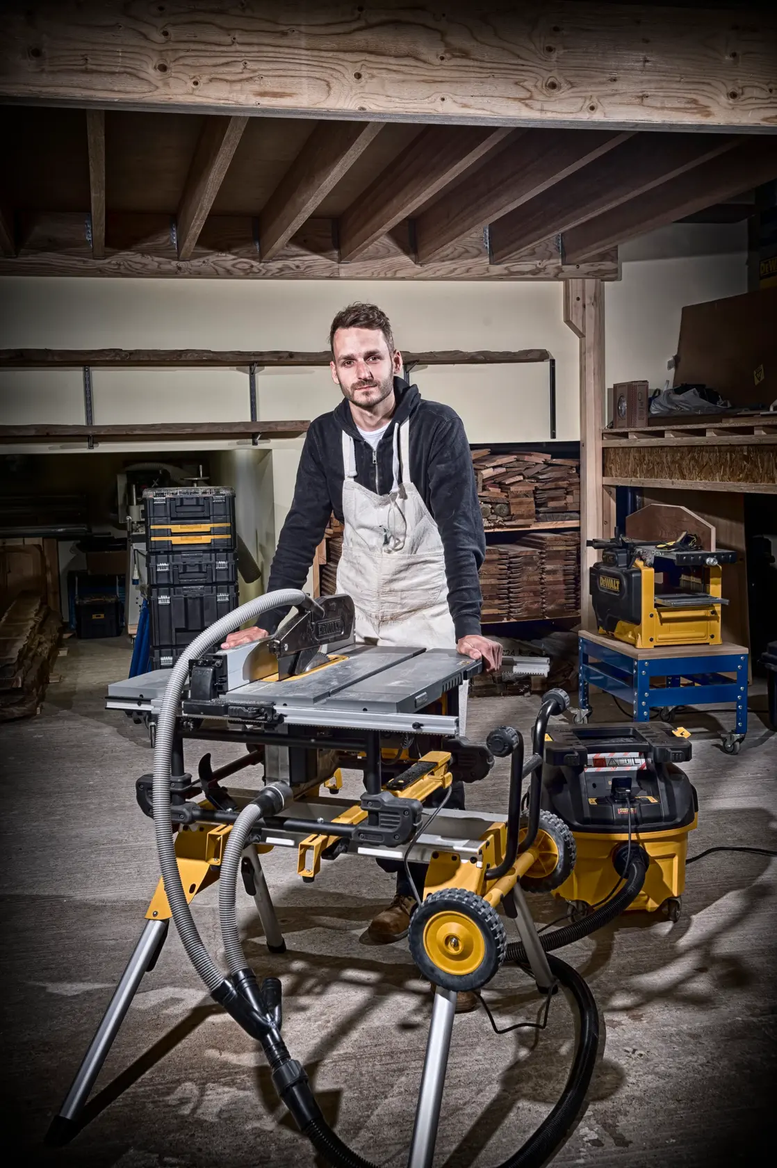 Person in workshop with DEWALT DT4351 saw on a stand and dust extraction system, surrounded by wood and tools.