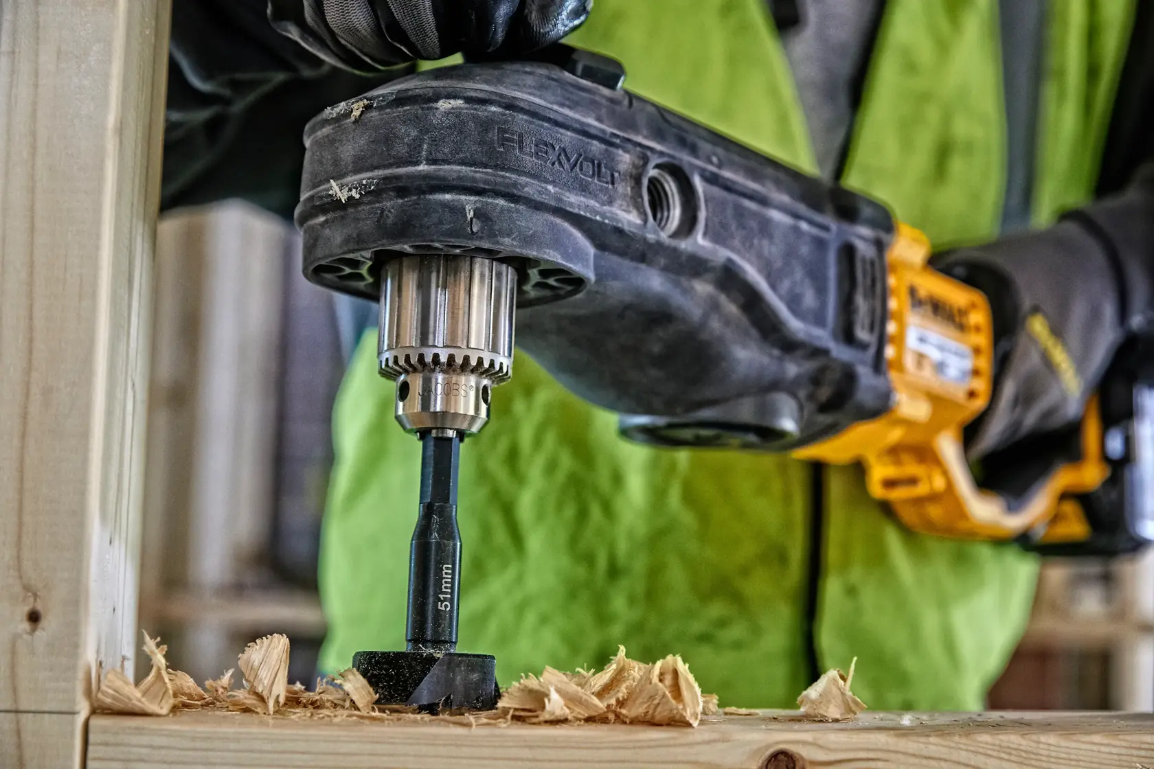 Trapano DEWALT in uso con punta per legno e trucioli, persona con guanti e gilet di sicurezza.