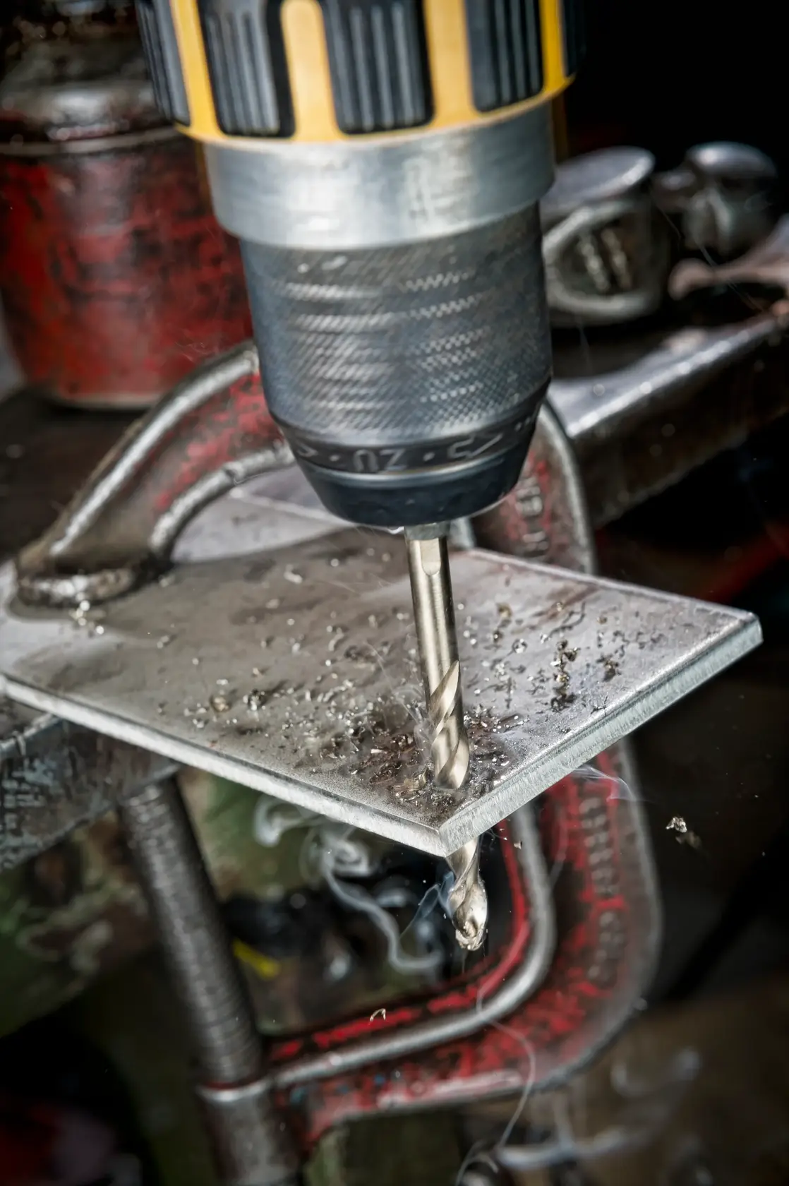 A DEWALT drill bit is used on a metal sheet held by a clamp, with metal shavings produced during drilling.