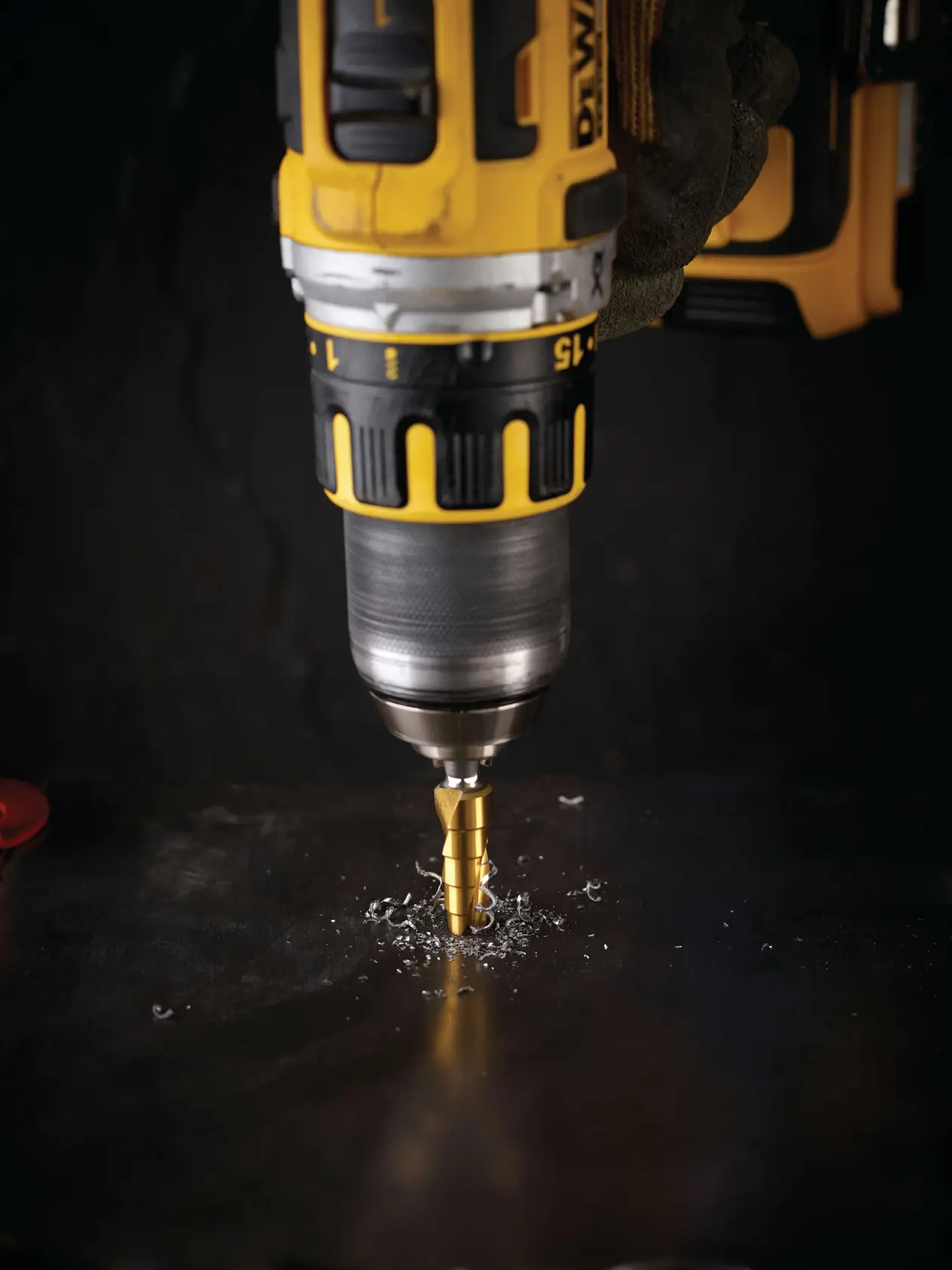 Trapano DEWALT con punta a gradini in uso su metallo, trucioli metallici visibili attorno alla punta.