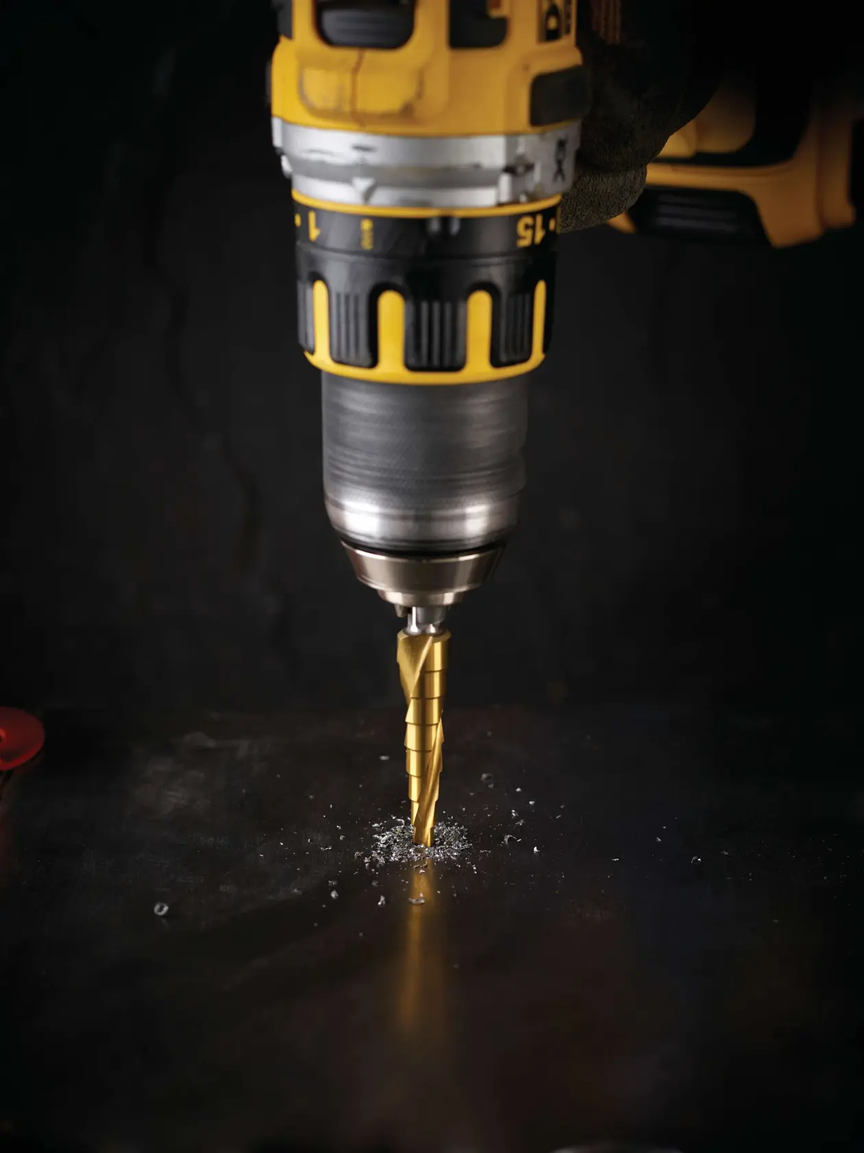 Trapano DEWALT con punta a gradini fora una superficie metallica scura producendo trucioli.