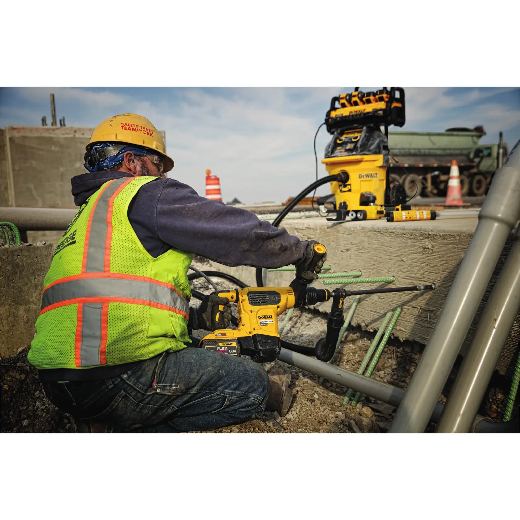 Worker uses DEWALT power tool to drill concrete at construction site. Safety gear and equipment are visible.