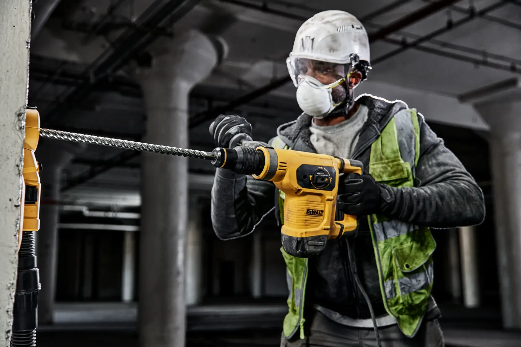 Worker uses DEWALT drill DT60820, DT60820-QZ on concrete; construction indoors, safety gear worn.