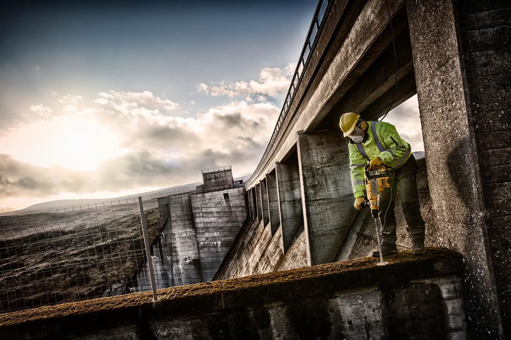 DEWALT DT60835 drill bit in use at a construction site. Worker wearing safety gear outdoors near buildings.