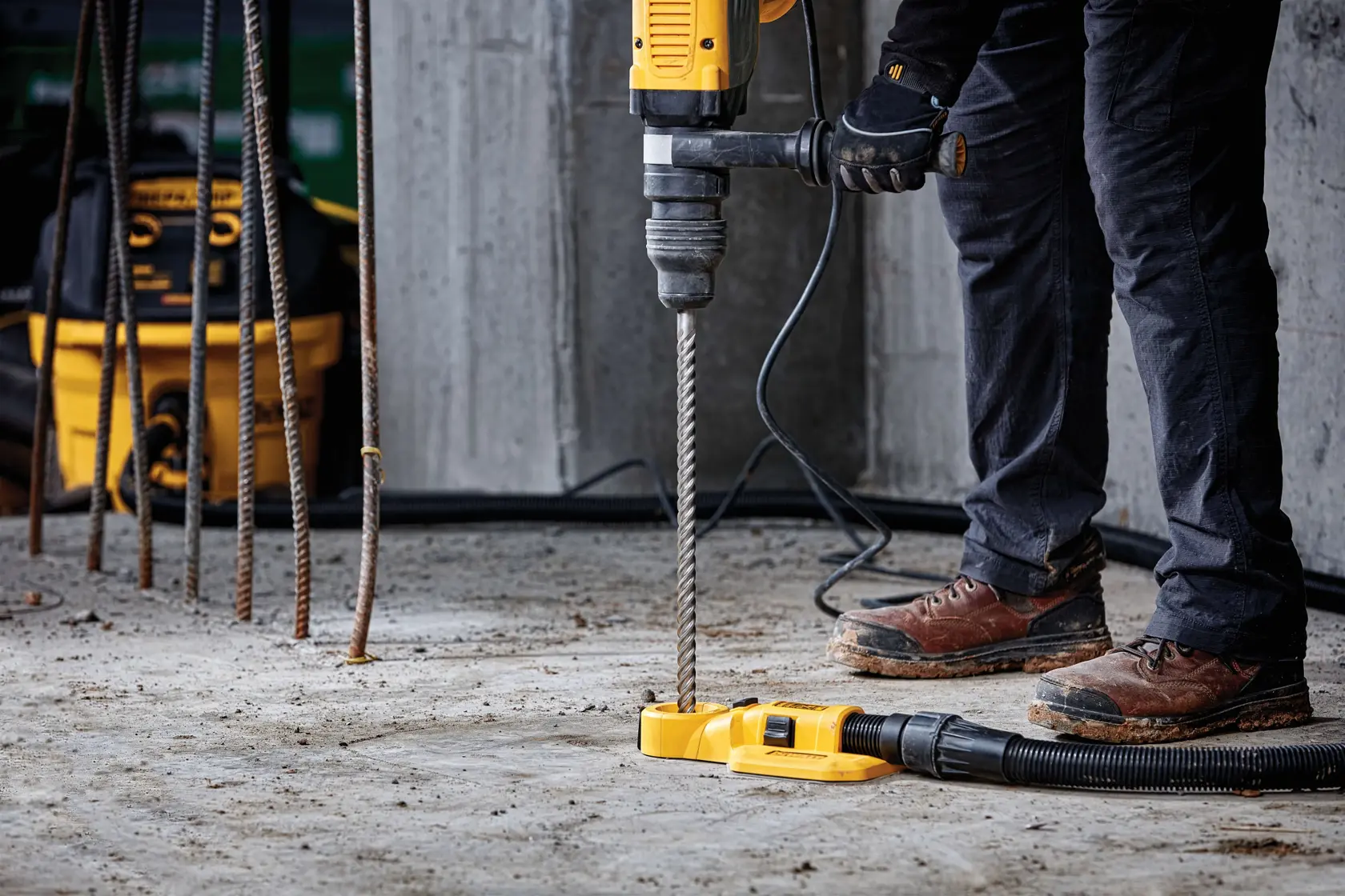 Worker drilling into concrete with a yellow DEWALT rotary hammer drill at a construction site.
