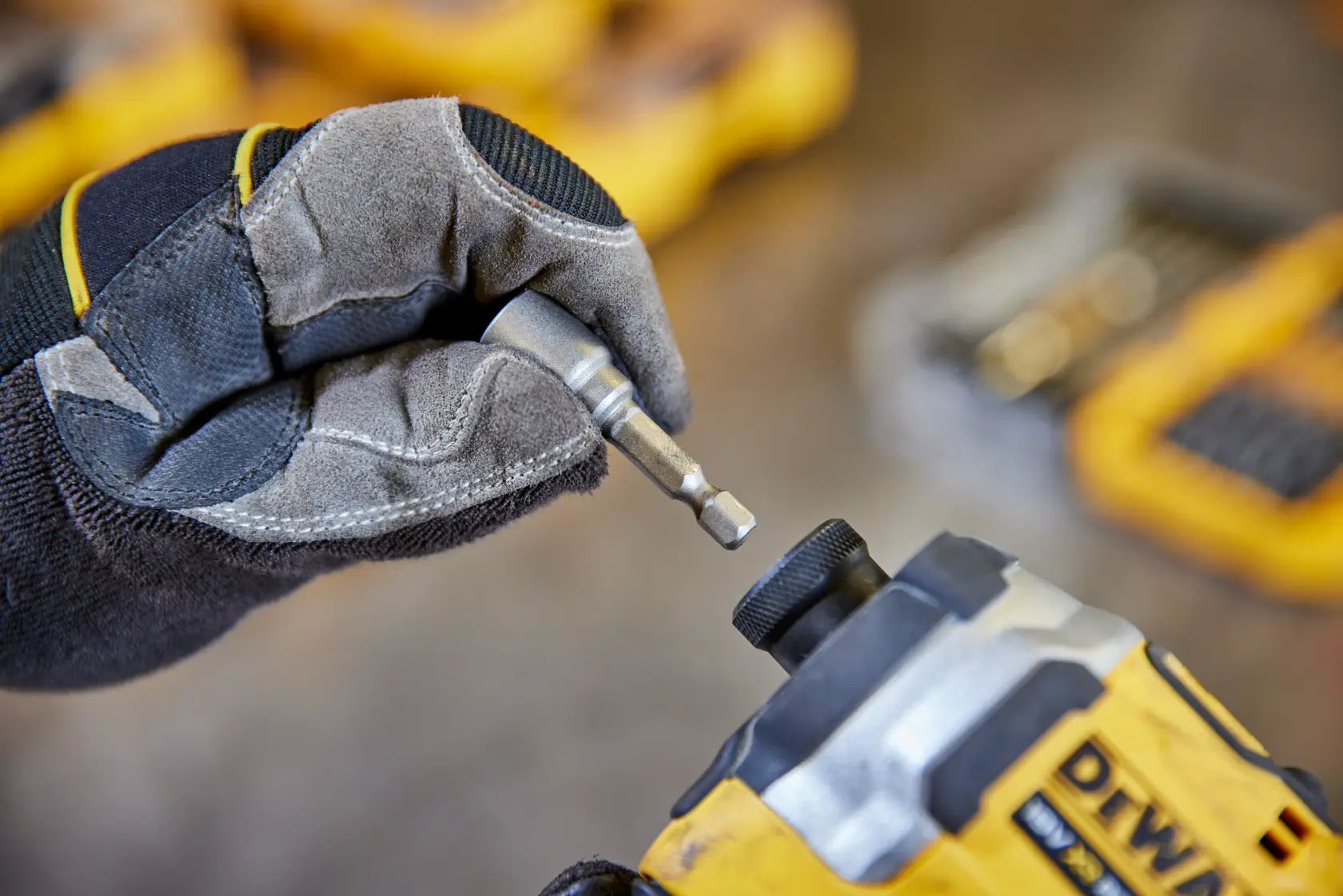 Mano con guanto inserisce una punta DEWALT in utensile elettrico giallo. Kit sfocati sullo sfondo.