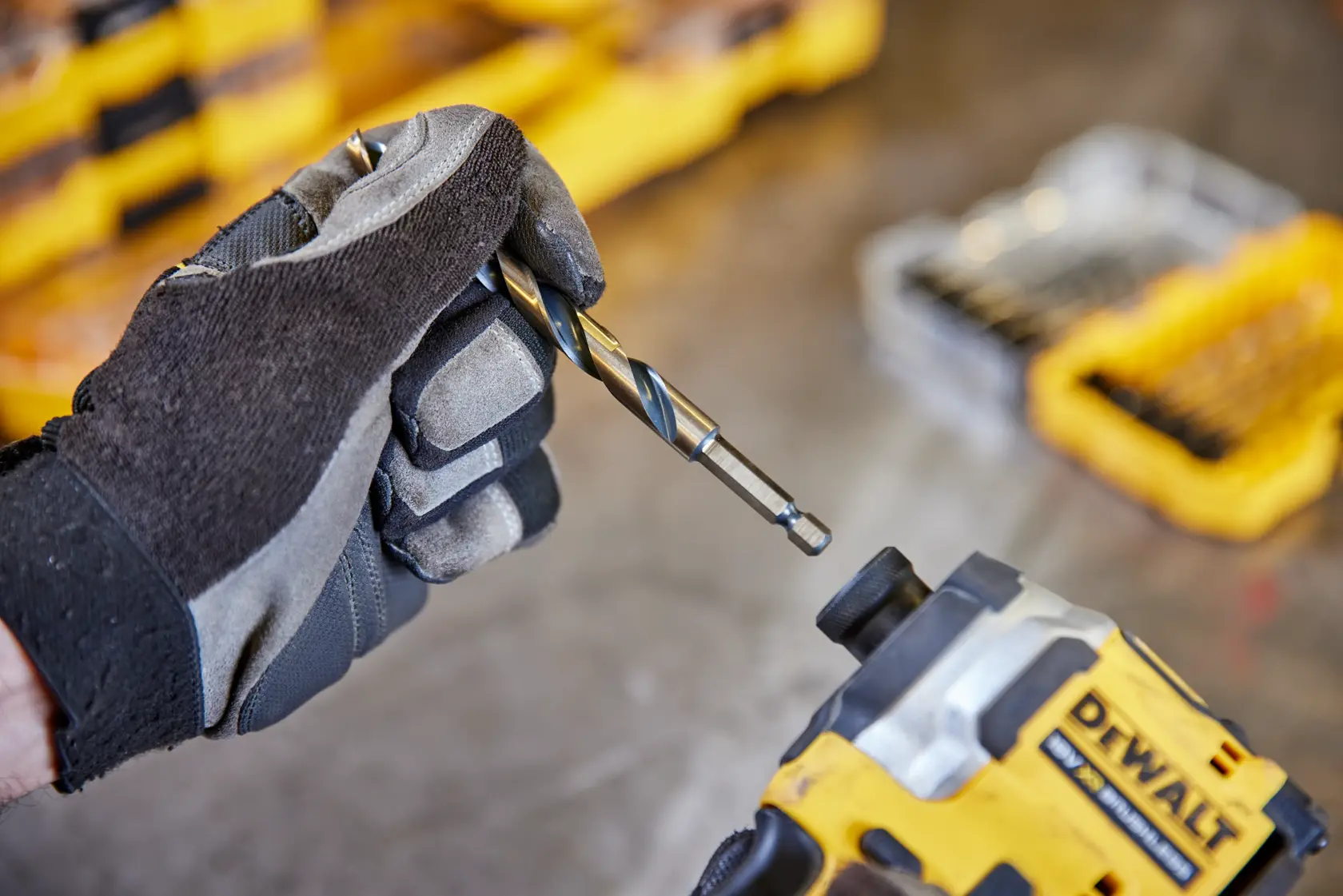 Mano guantata tiene una punta vicino utensile DEWALT con scatola gialla sullo sfondo.
