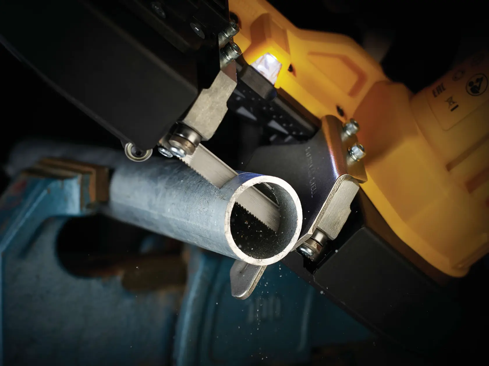 Primo piano di una sega DEWALT che taglia un tubo metallico tenuto in una morsa.