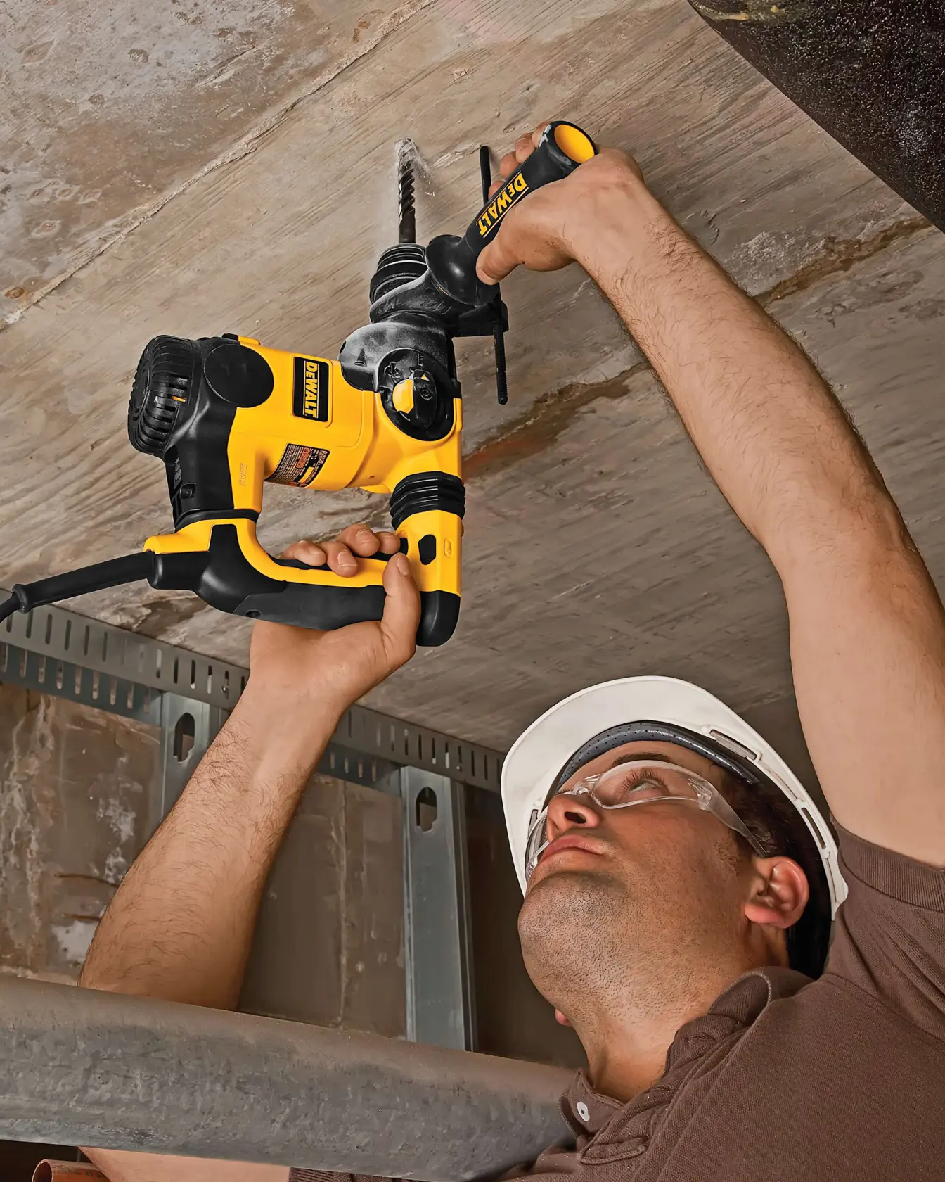 Person uses DEWALT DT8913 rotary drill to bore into concrete ceiling while wearing a safety helmet.