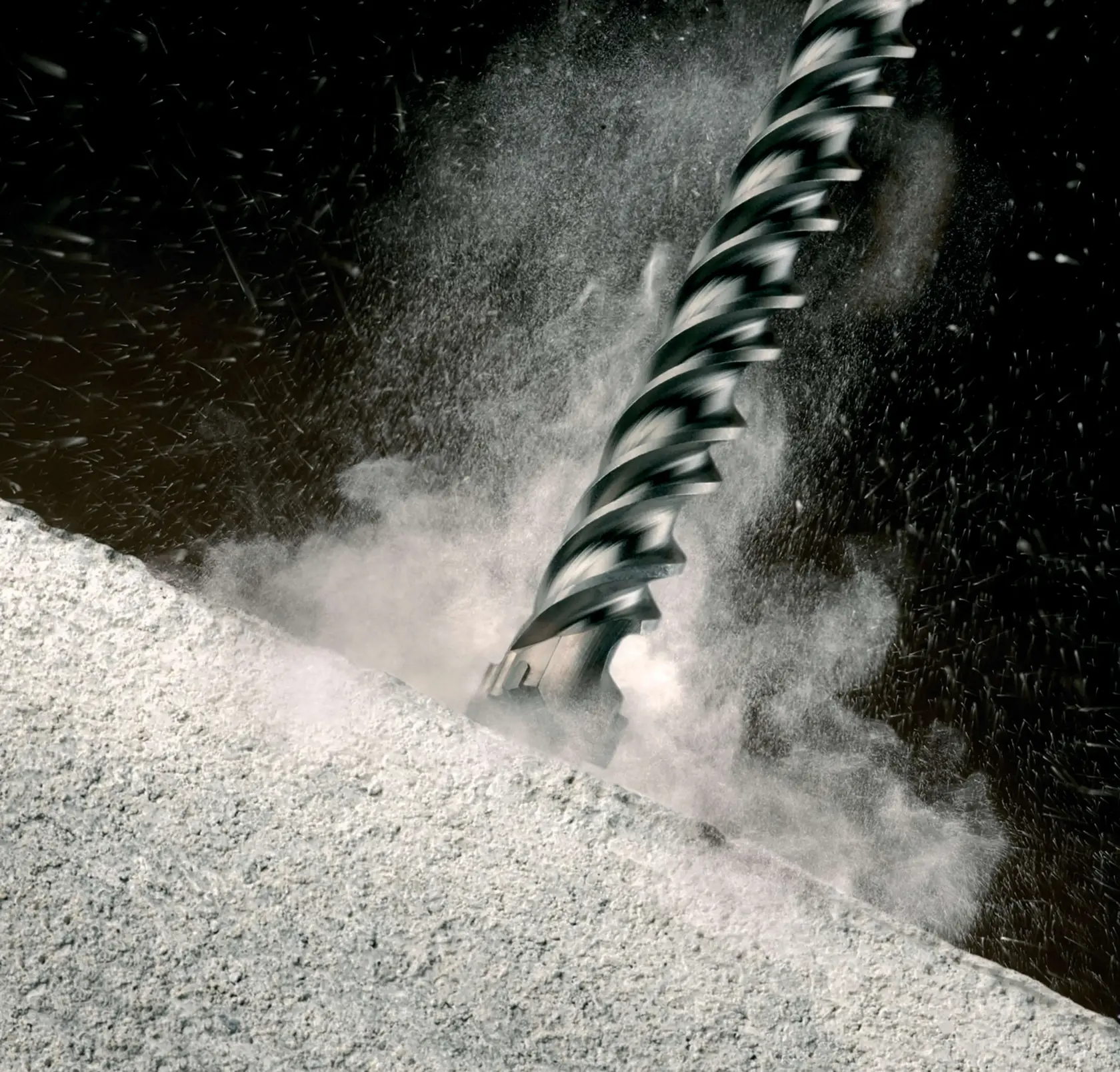 Close-up of a DEWALT drill bit cutting into concrete, with dust and debris flying.