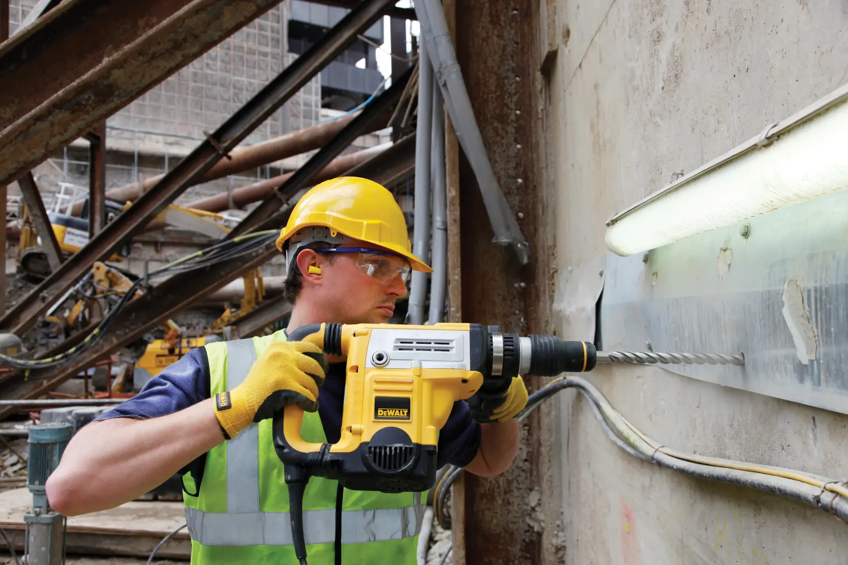 Worker uses a DEWALT rotary hammer drill on a concrete wall at a construction site.