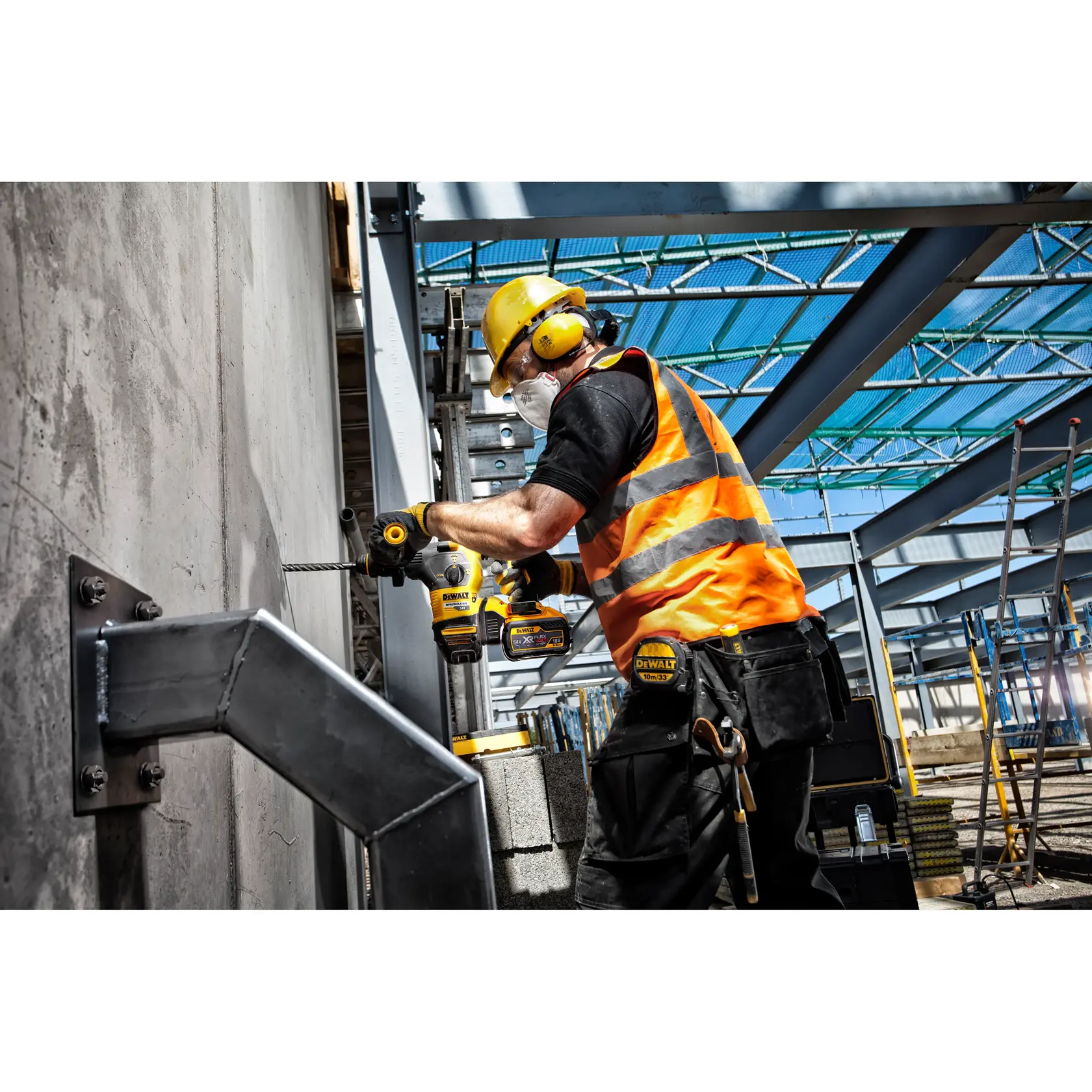 Worker using a DEWALT drill on a concrete wall at a construction site, wearing safety gear and a high-visibility vest.