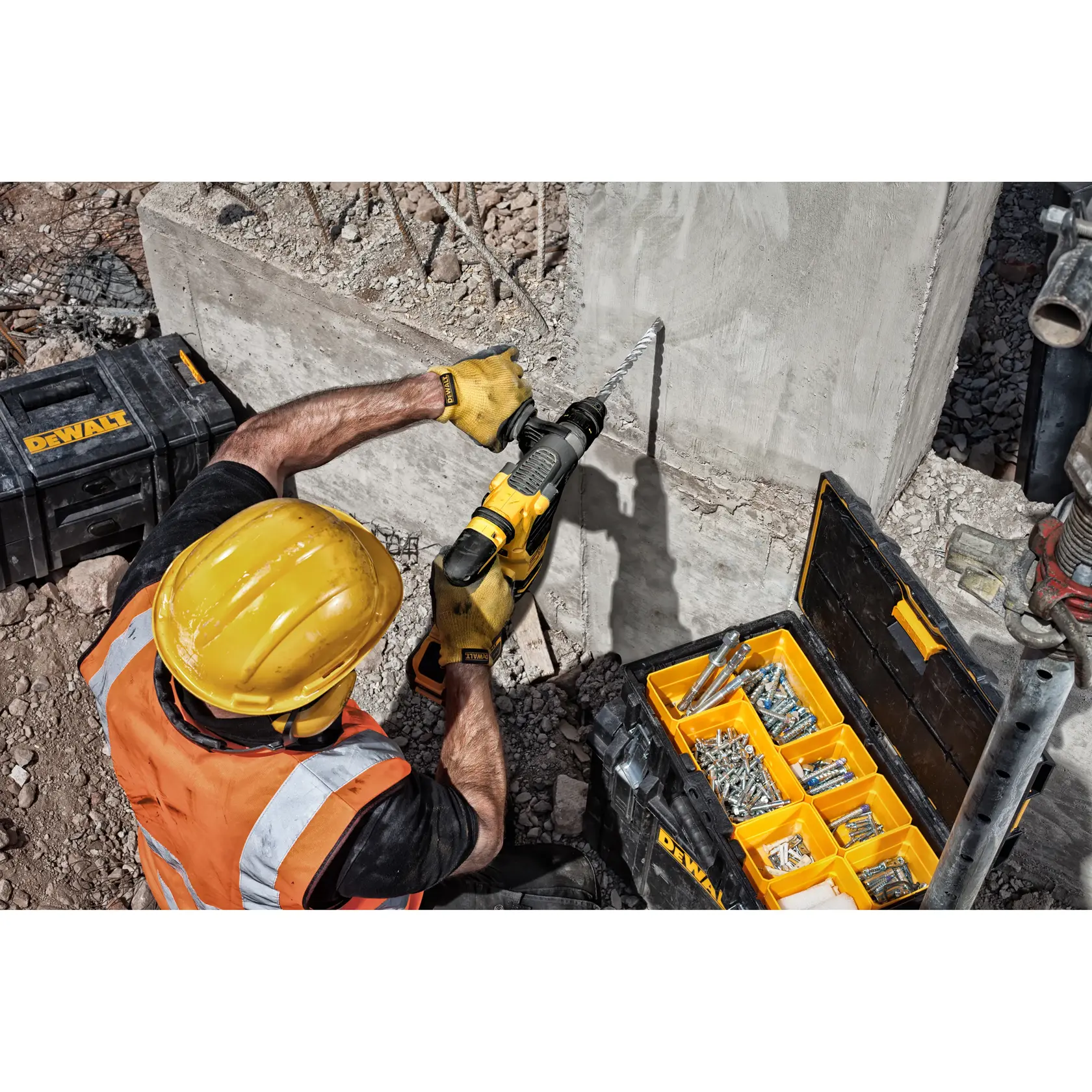 Worker drills into concrete with a DEWALT tool, next to a toolbox with assorted screws and anchors.