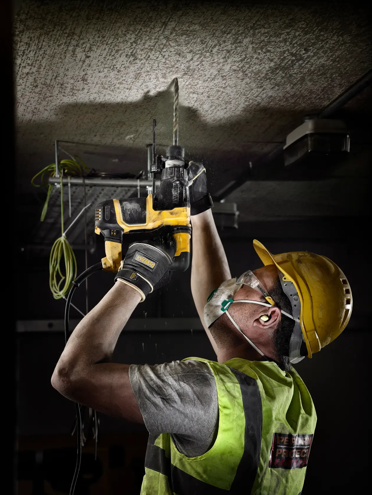 Trabajador perfora techo con taladro DEWALT, lleva casco y equipo de seguridad en obra.
