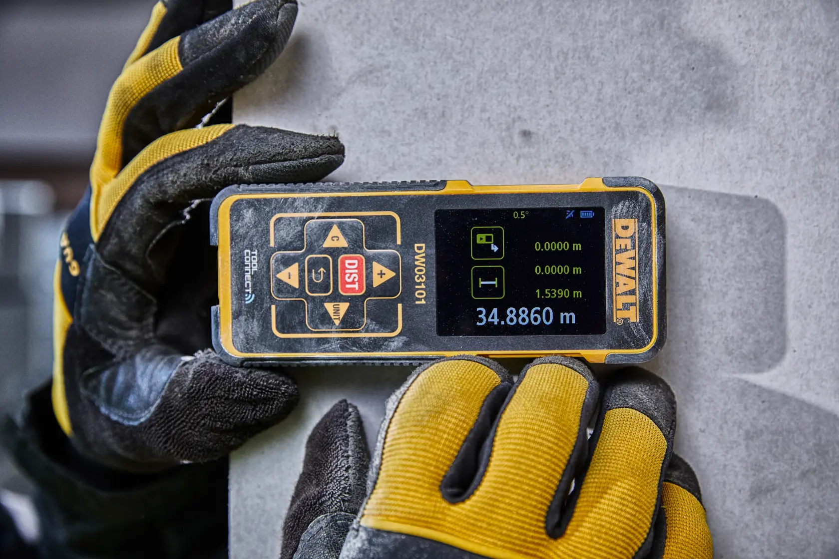 Gloved hands hold a DEWALT DW03101 laser distance meter, displaying measurements on a digital screen.