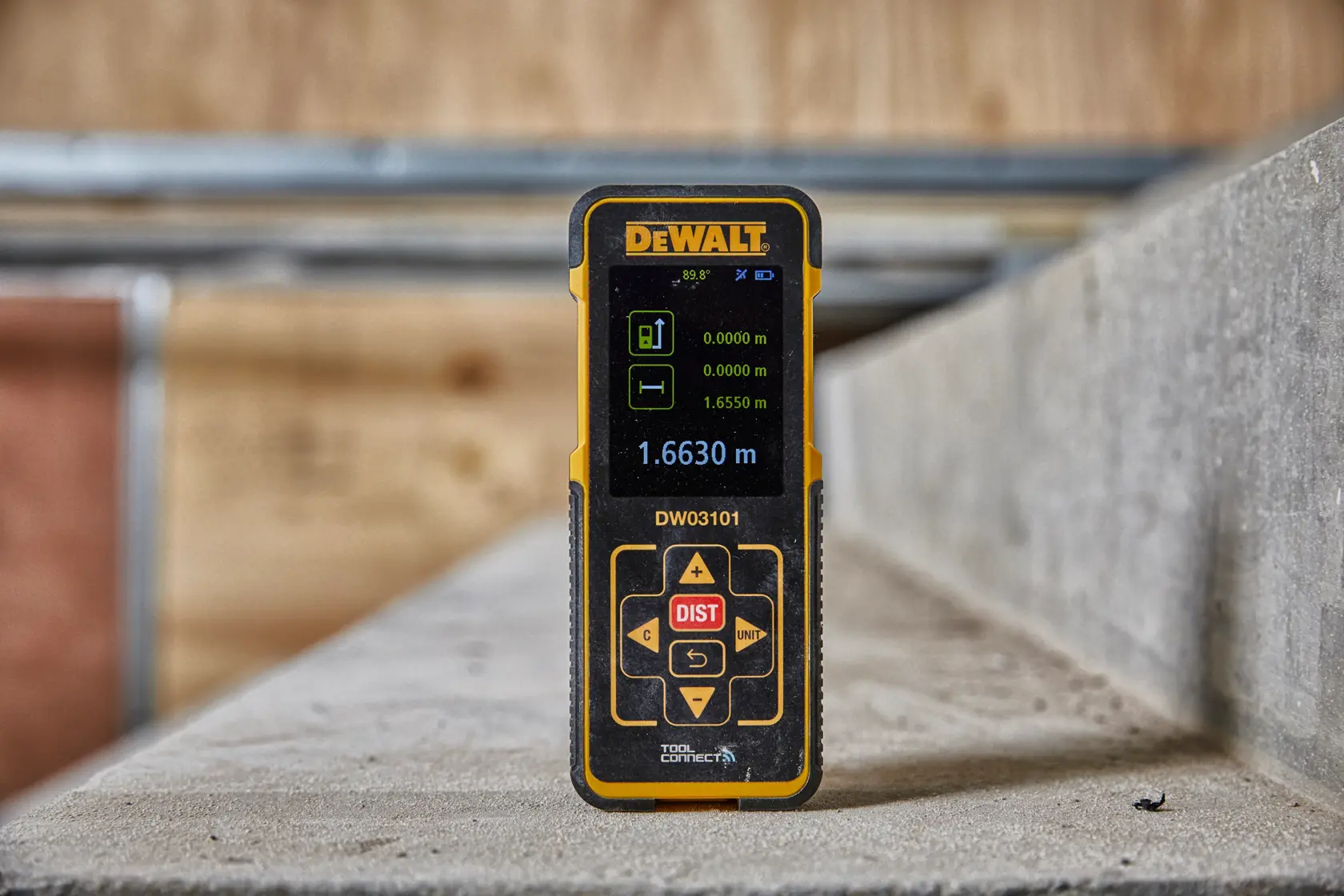 DEWALT DW03101 digital laser distance measurer on a concrete surface in a workshop setting.