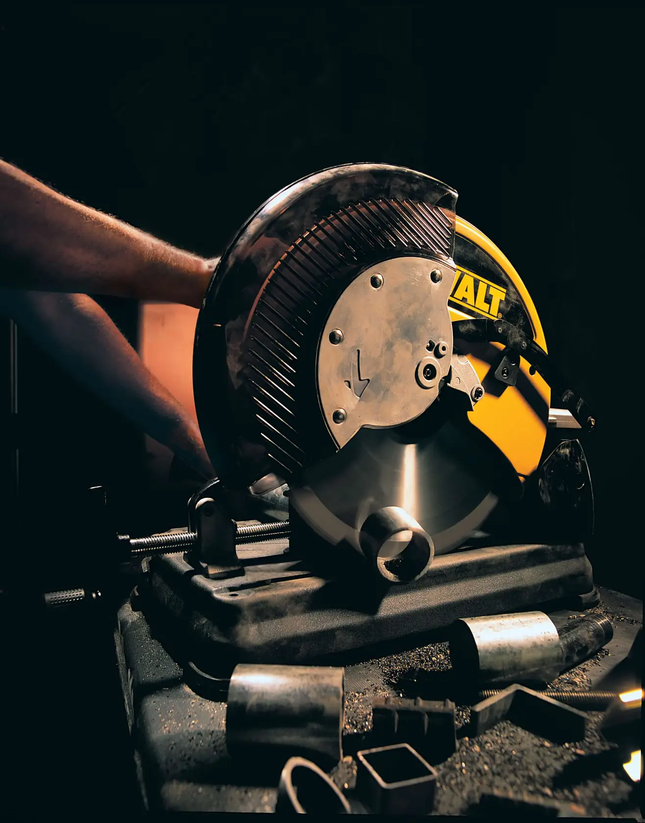 DEWALT DW872 cutting machine slicing metal pipes in a workshop, with scattered metal pieces on the surface.