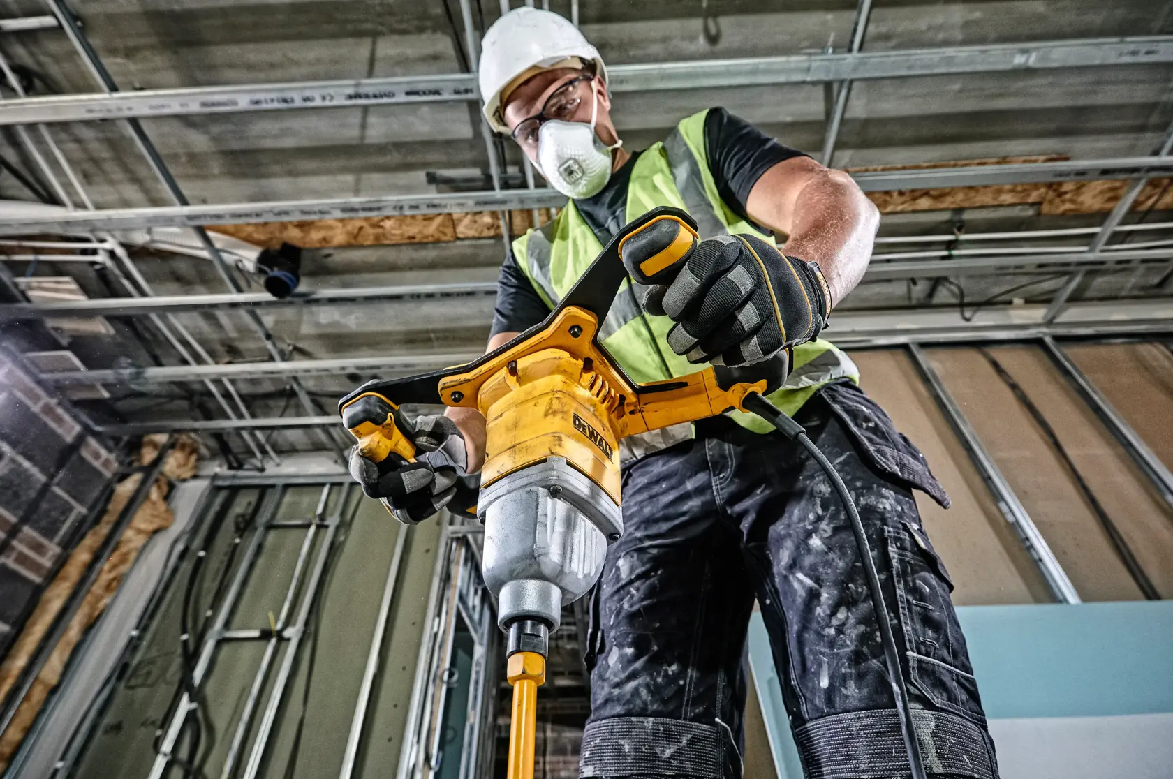 Person using DEWALT DWD241 mixer drill at a construction site, wearing safety gear and gloves.