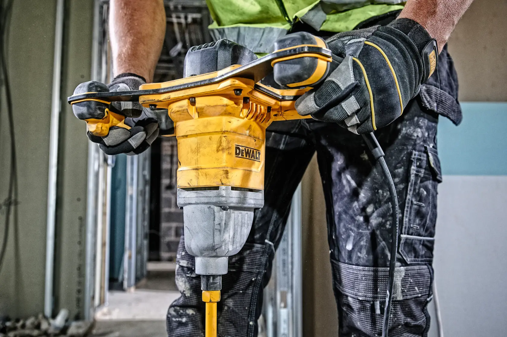 Person operating a DEWALT DWD241 mixer drill on a construction site, wearing gloves and workwear.