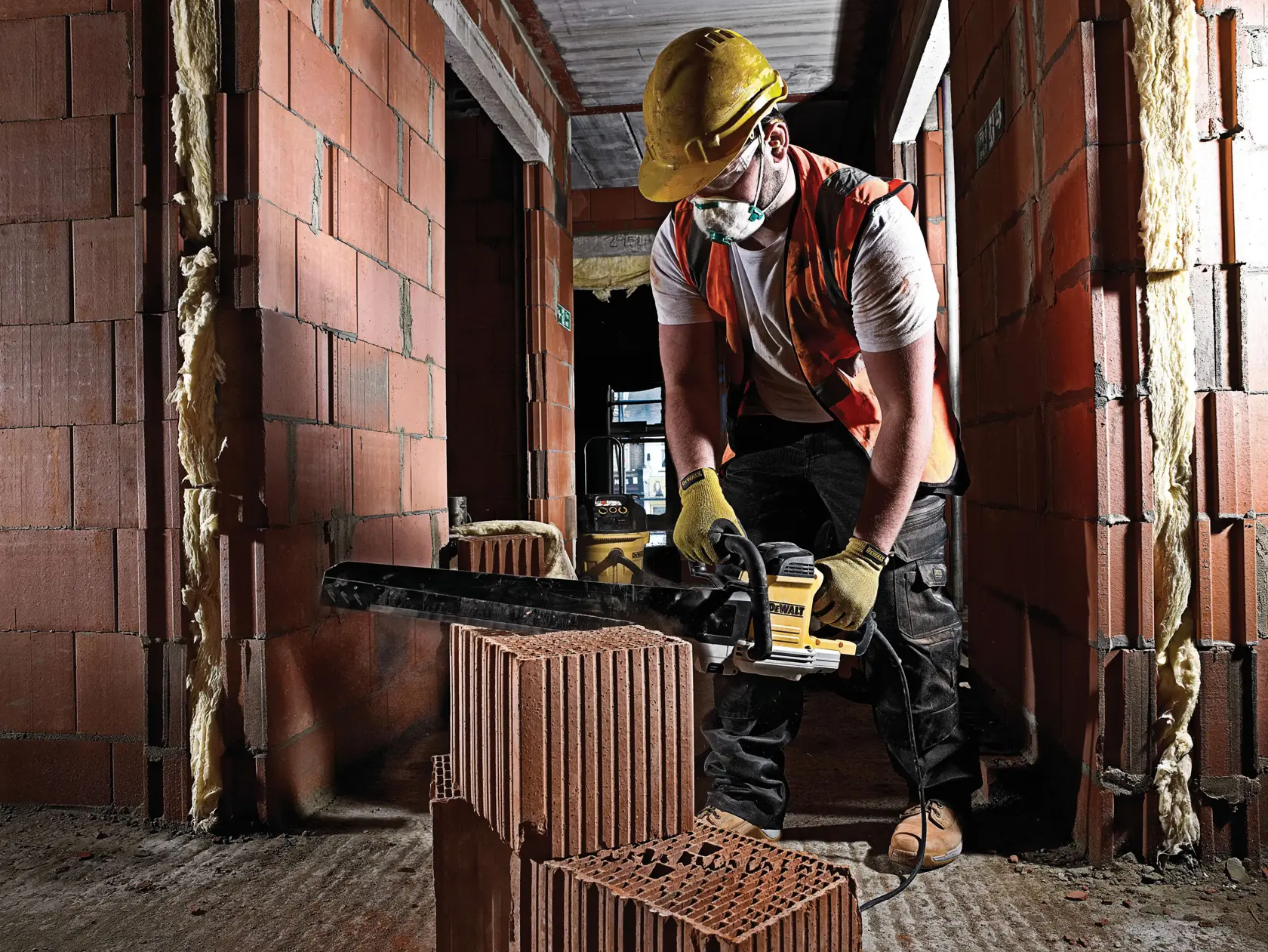Worker uses DEWALT saw to cut brick at a construction site, wearing safety gear and gloves for protection.