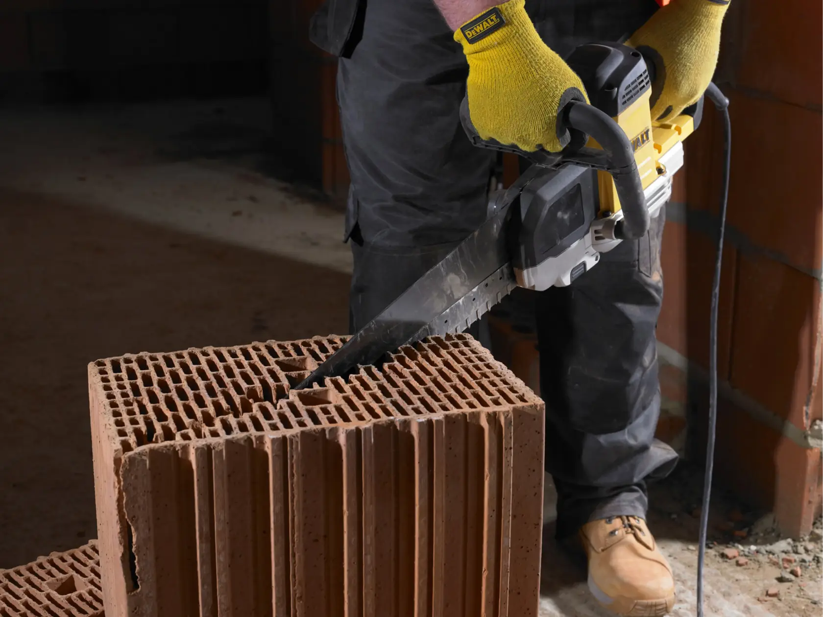 Person uses a DEWALT saw to cut a large hollow brick, wearing gloves, indoors at a construction site.