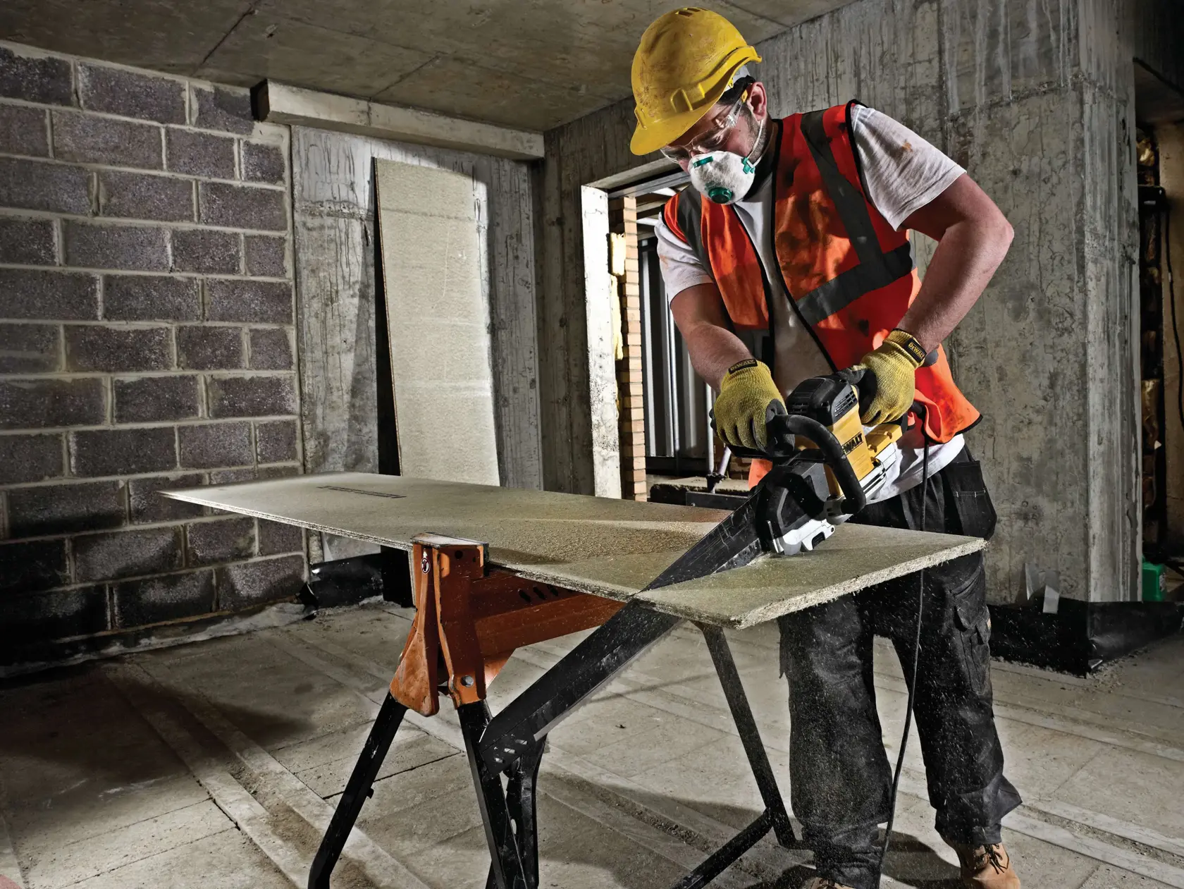 Construction worker using a DEWALT saw to cut a board on a stand in an unfinished indoor space.
