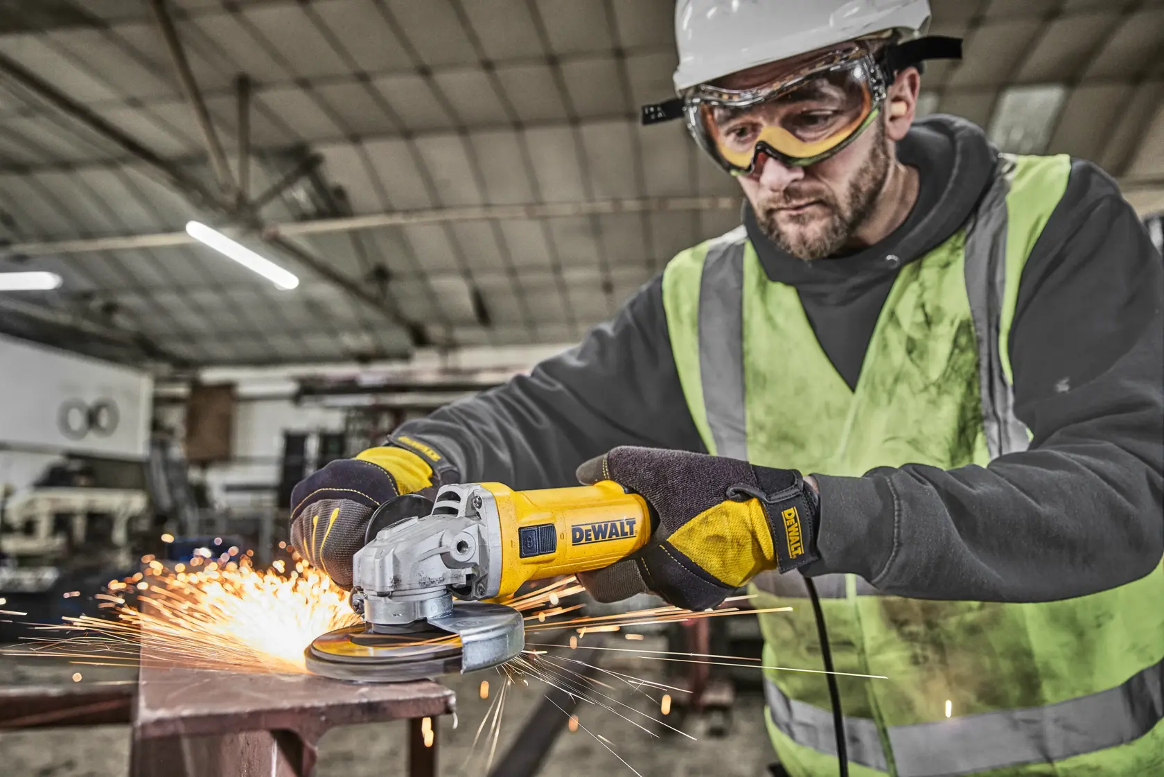 Worker using DEWALT DWE4036 angle grinder, producing sparks on metal in an industrial workshop.