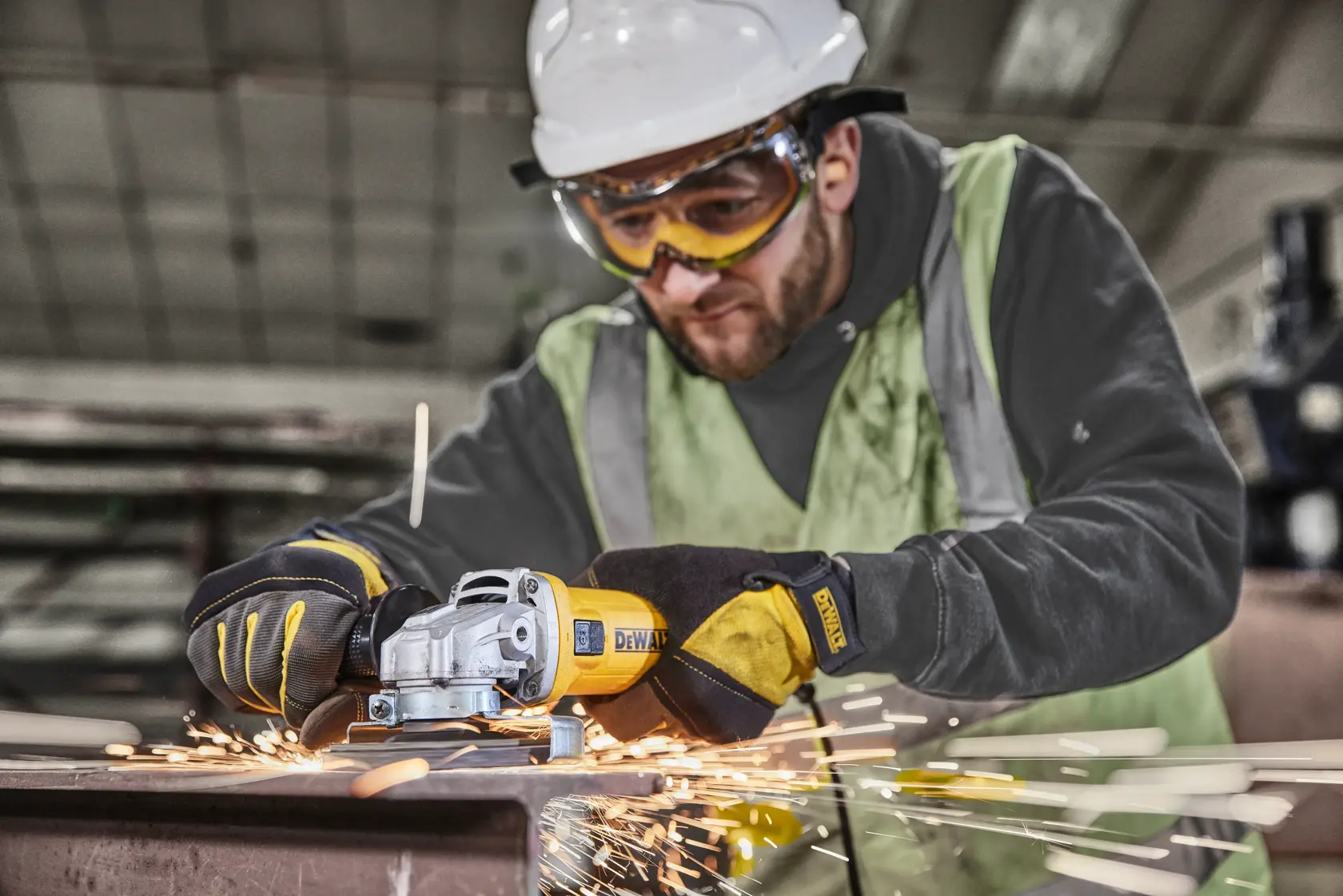 Worker uses DEWALT DWE4036 angle grinder on metal, gloves and sparks visible in industrial setting.