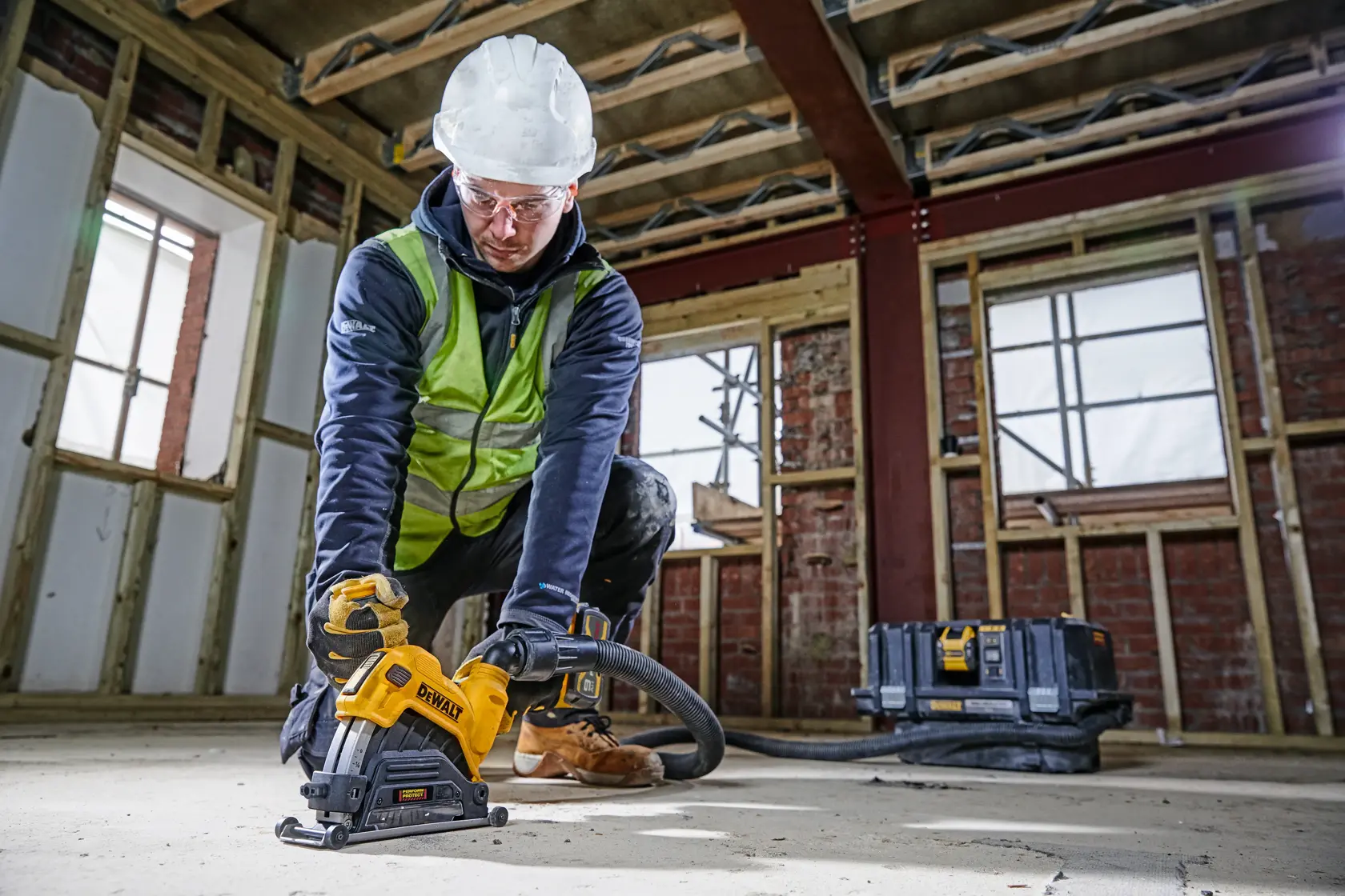 Worker using DEWALT DWE46225 saw at a construction site, wearing safety gear and cutting concrete floor.