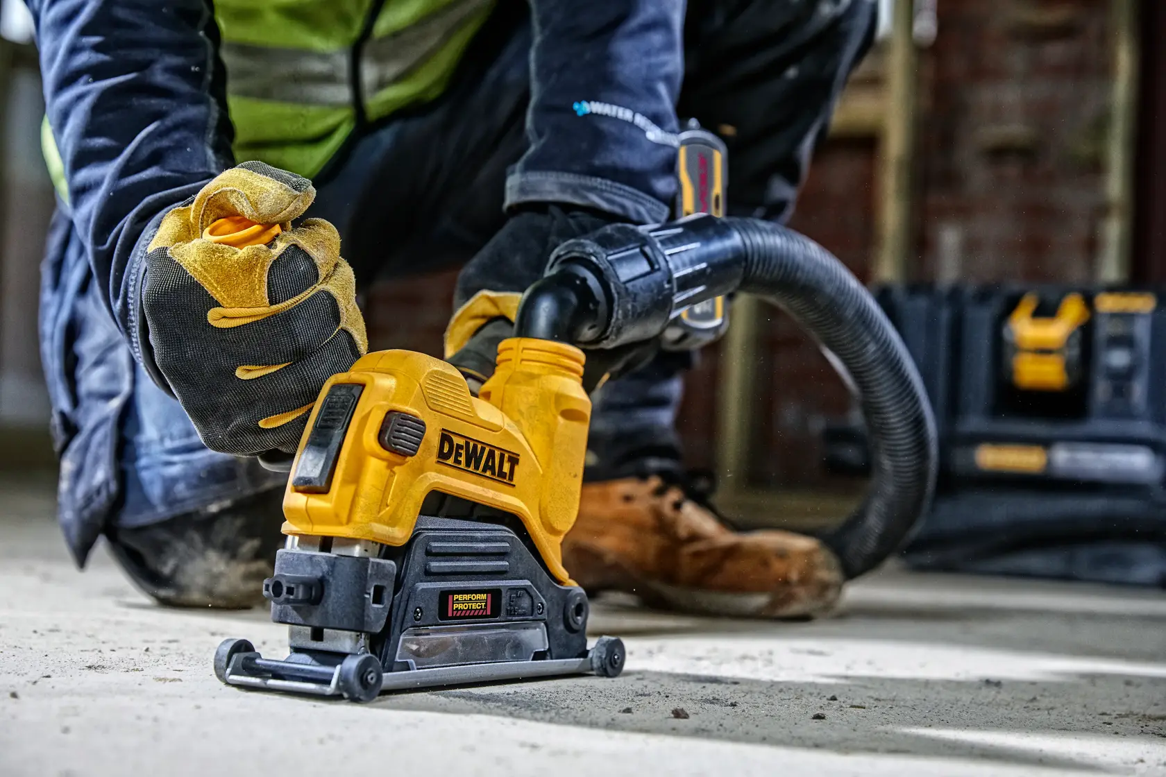 Worker uses DEWALT DWE46225 power tool with dust extractor on concrete floor at a construction site.