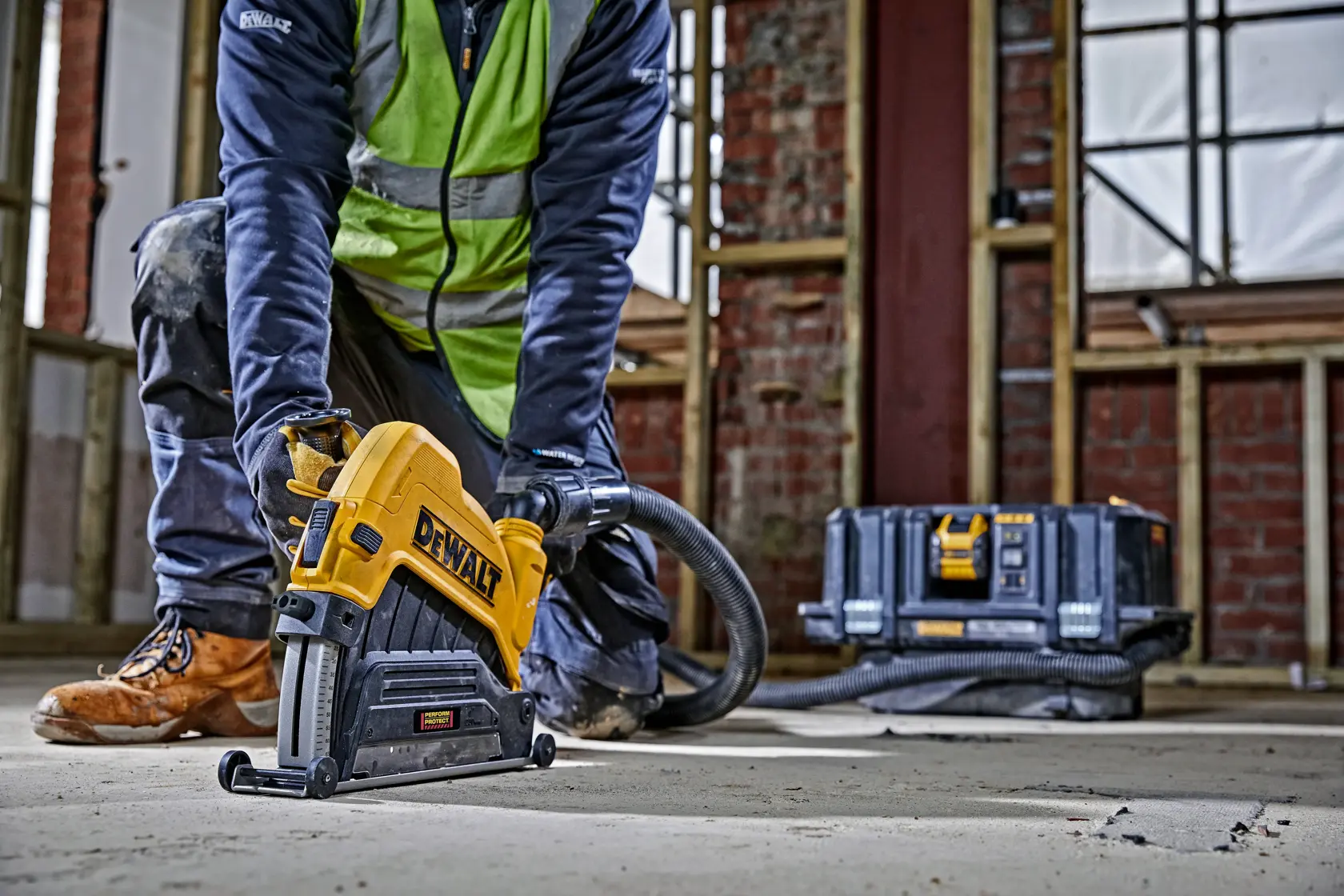 Persona usa scanalatrice DEWALT su pavimento di cemento in cantiere. Valigetta visibile dietro.