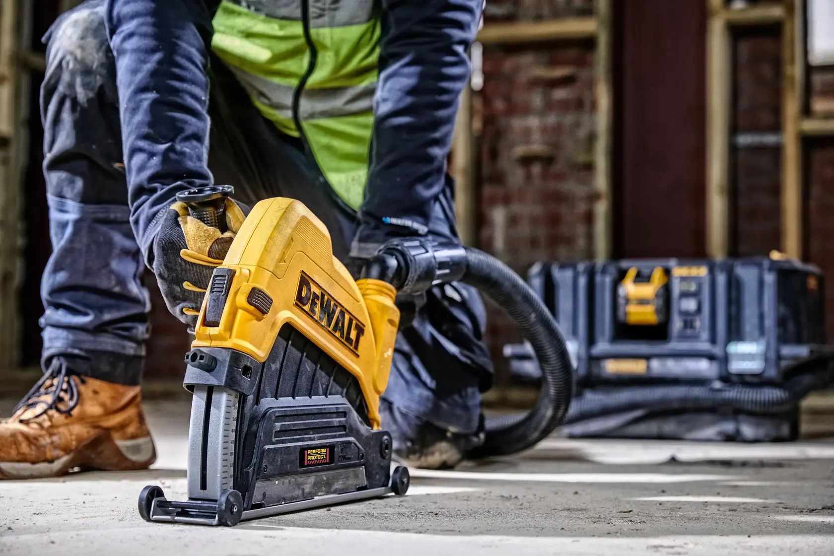 Operaio usa utensile DEWALT sul pavimento; valigetta e tubo visibili sullo sfondo.